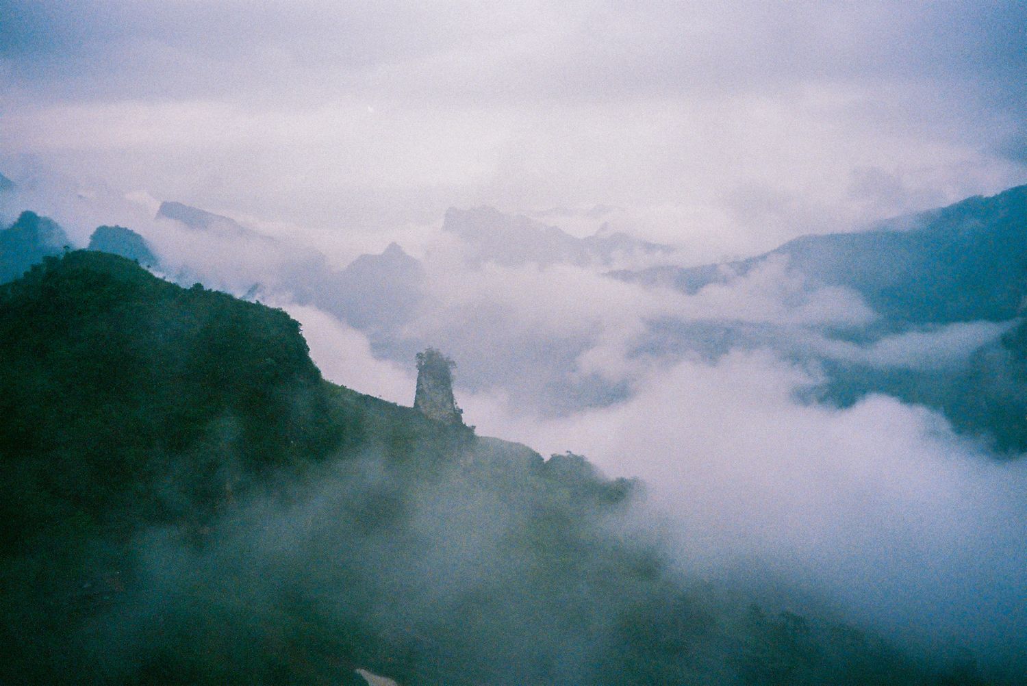 Misty mountain peaks emerge through dramatic clouds with a silhouetted tower visible against the moody sky.