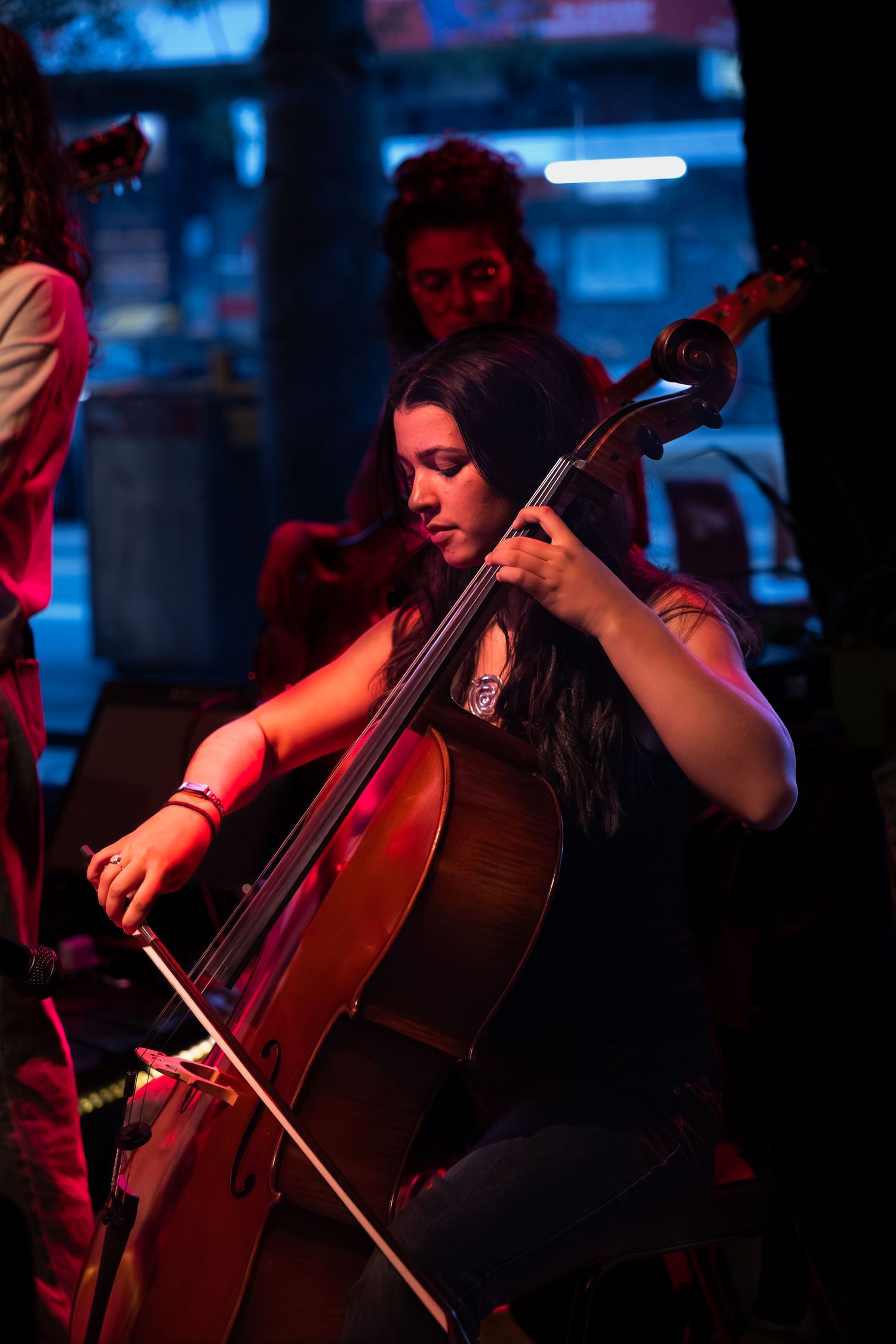 Cellist performing on stage illuminated by dramatic blue and red lighting during a concert performance.