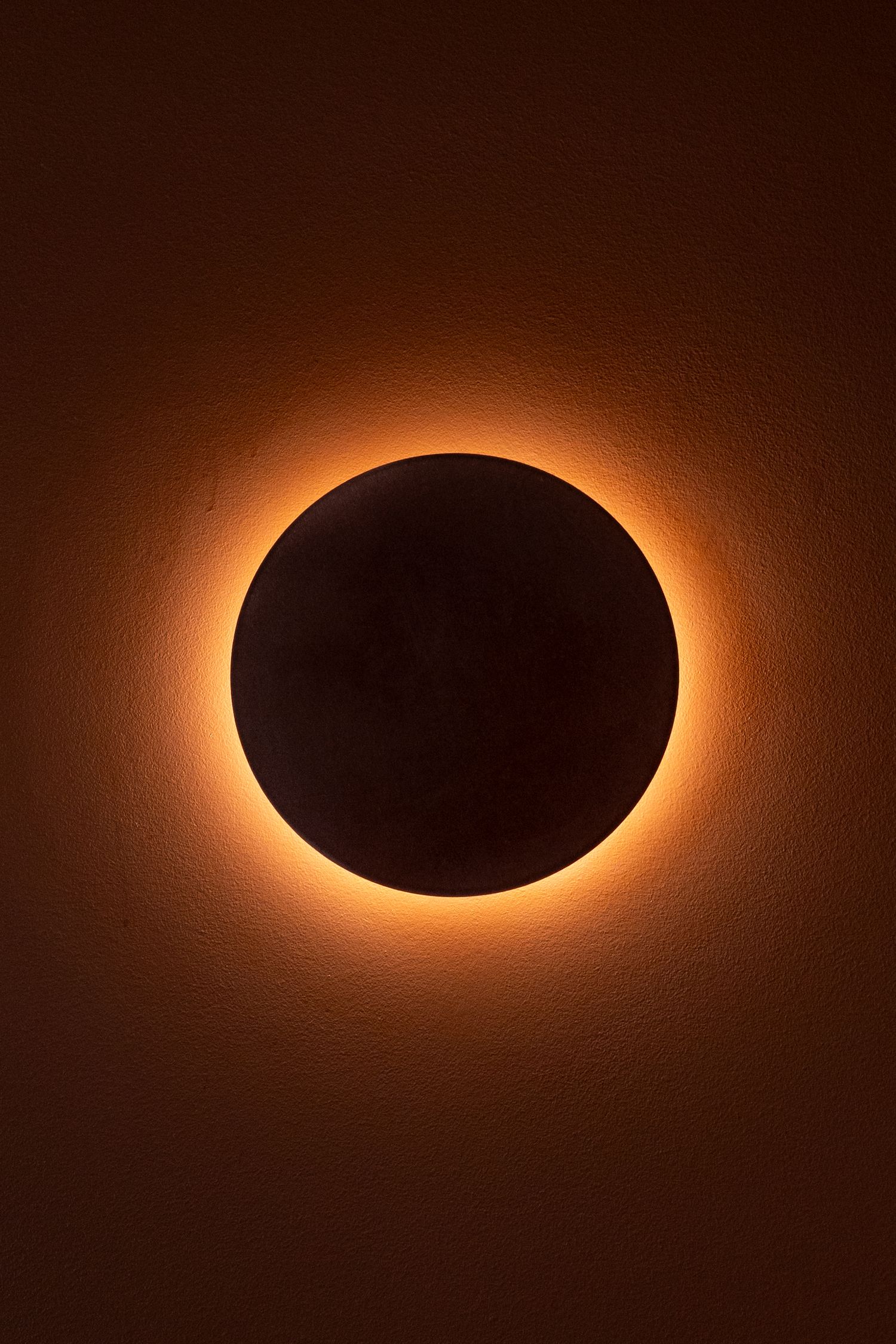 A stunning total solar eclipse with glowing orange corona surrounding the dark moon against a warm amber sky.