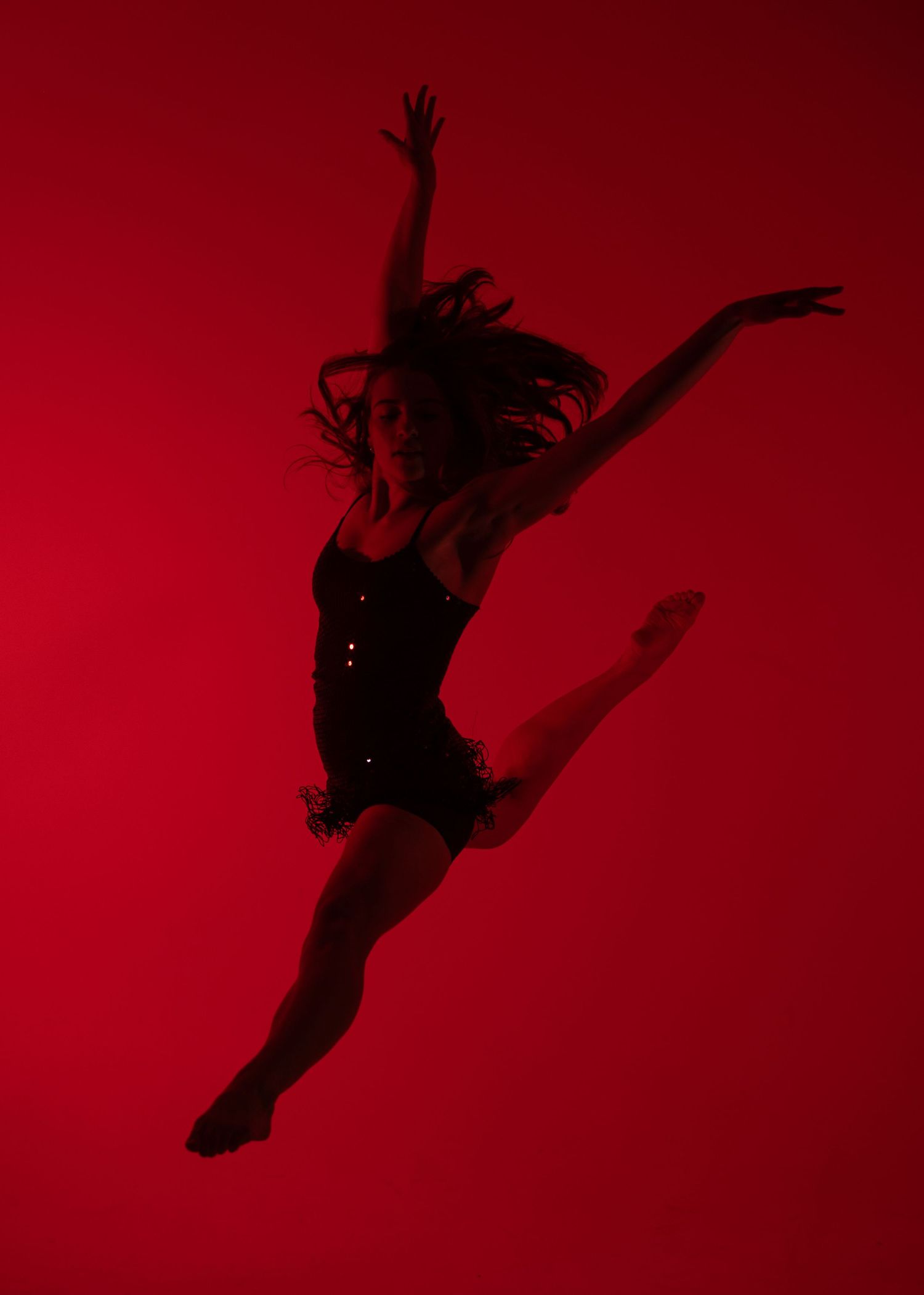 Dynamic female dancer leaps mid-air in a black outfit against a bold red background.