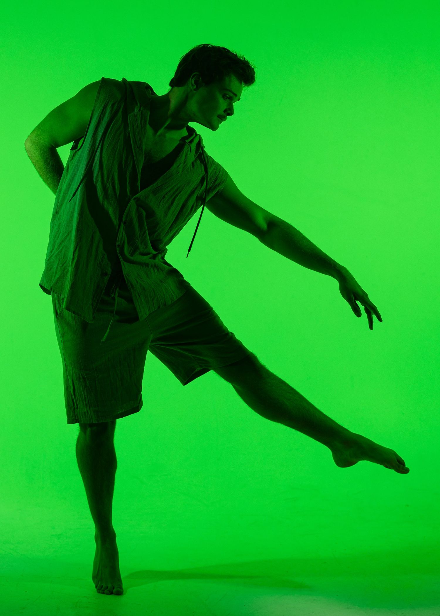 Male dancer performs an expressive contemporary dance move under dramatic green lighting on stage.
