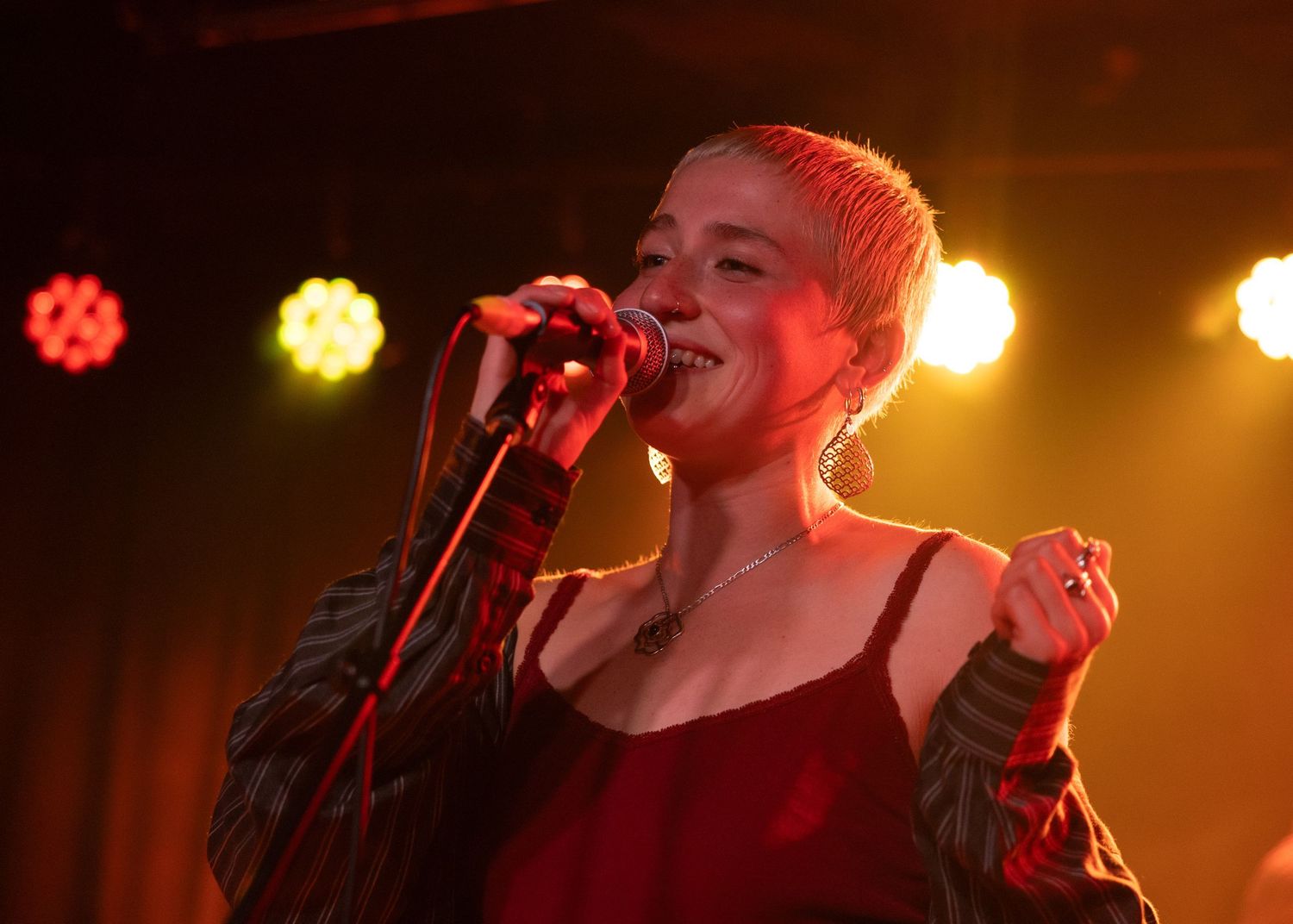 Female singer performing on stage under red and yellow stage lights, singing into a microphone at a live concert.