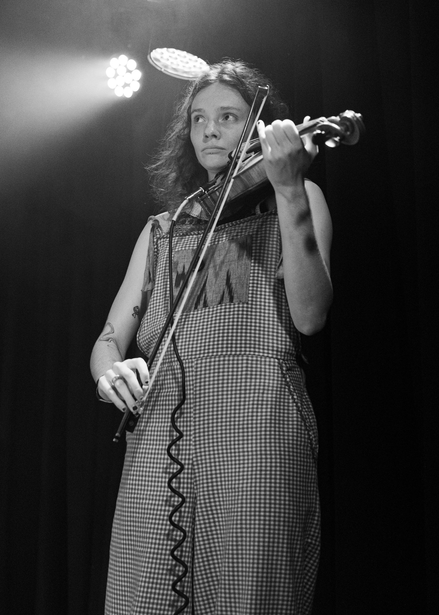 Woman playing violin on stage in black and white photo wearing houndstooth dress under spotlight.