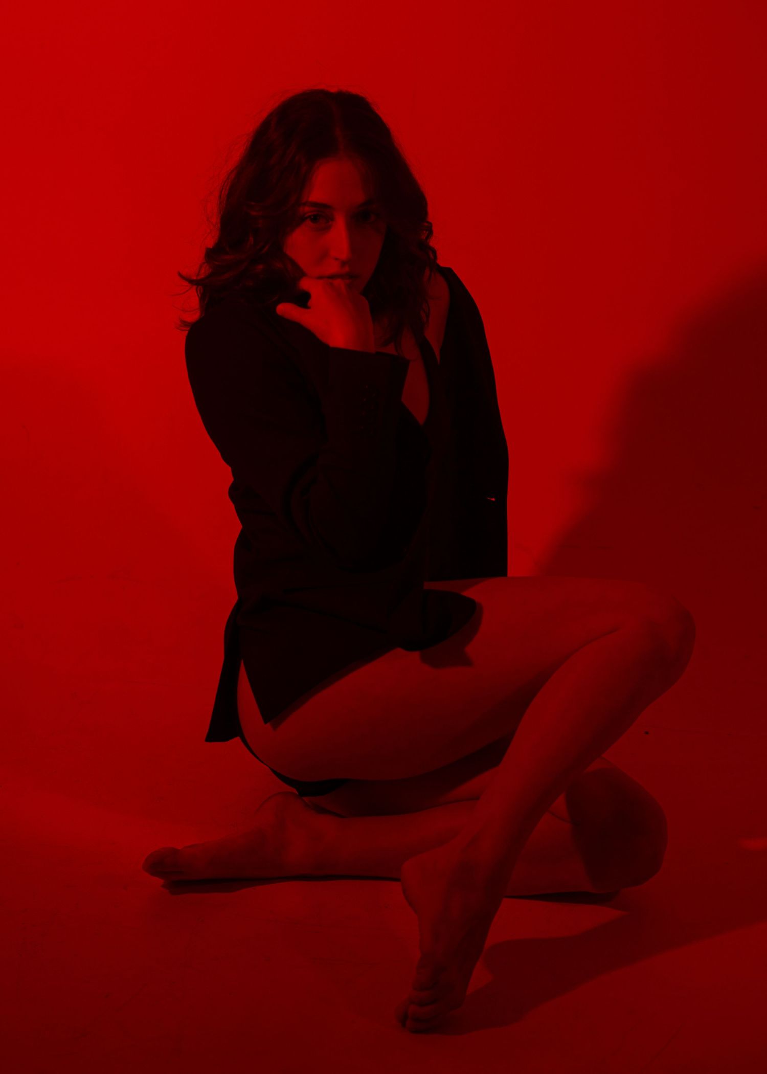Woman in black outfit posed against vibrant red background in dramatic studio photography.