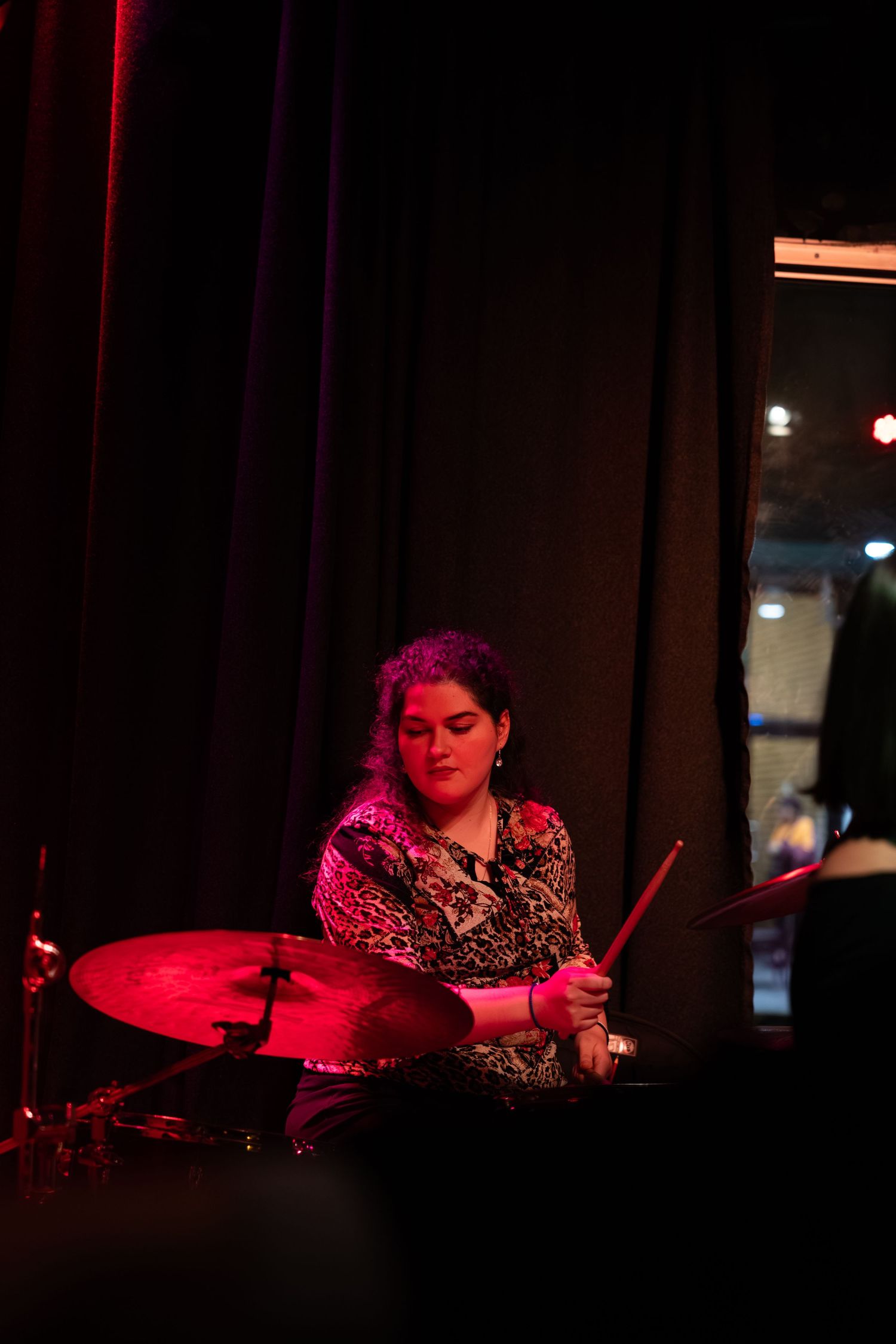 Drummer performing under dramatic red stage lighting in a dimly lit venue.