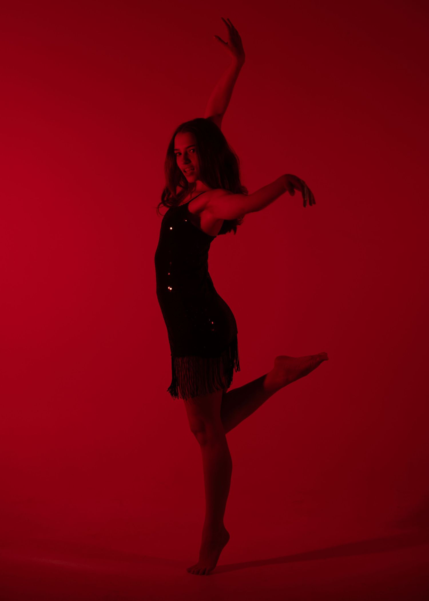Dancer performs an expressive contemporary dance pose in dramatic red lighting wearing a black sequin dress.