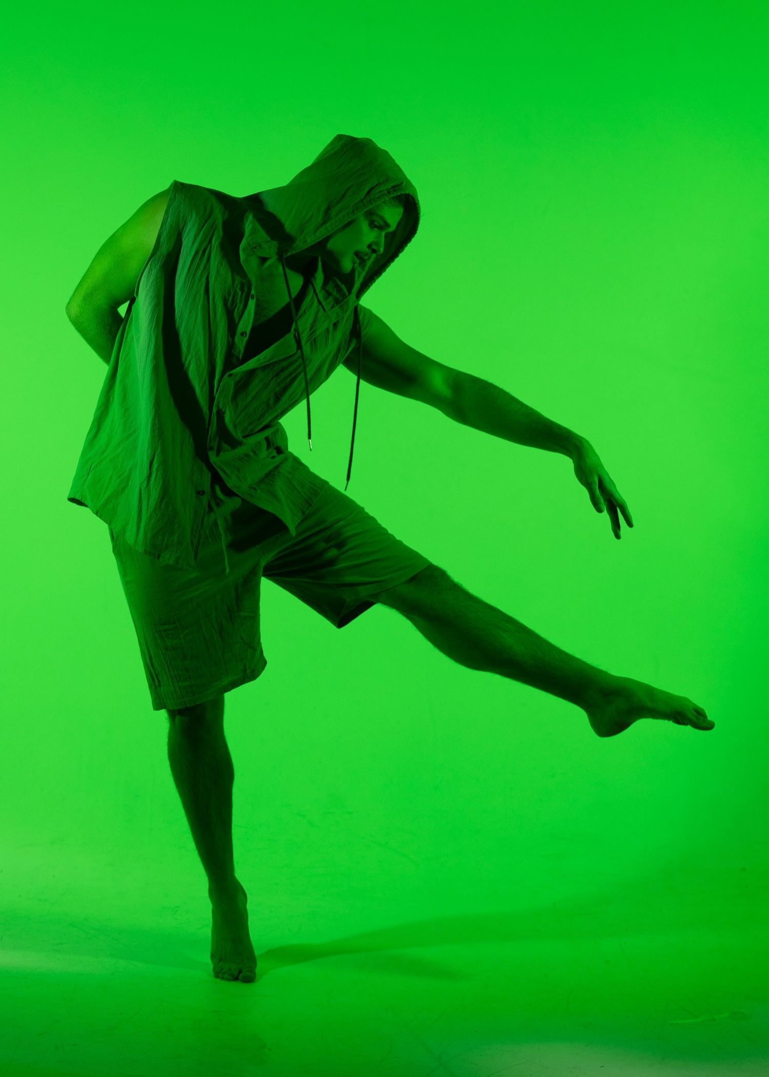 Male dancer performs dynamic kick pose bathed in vibrant green studio lighting.