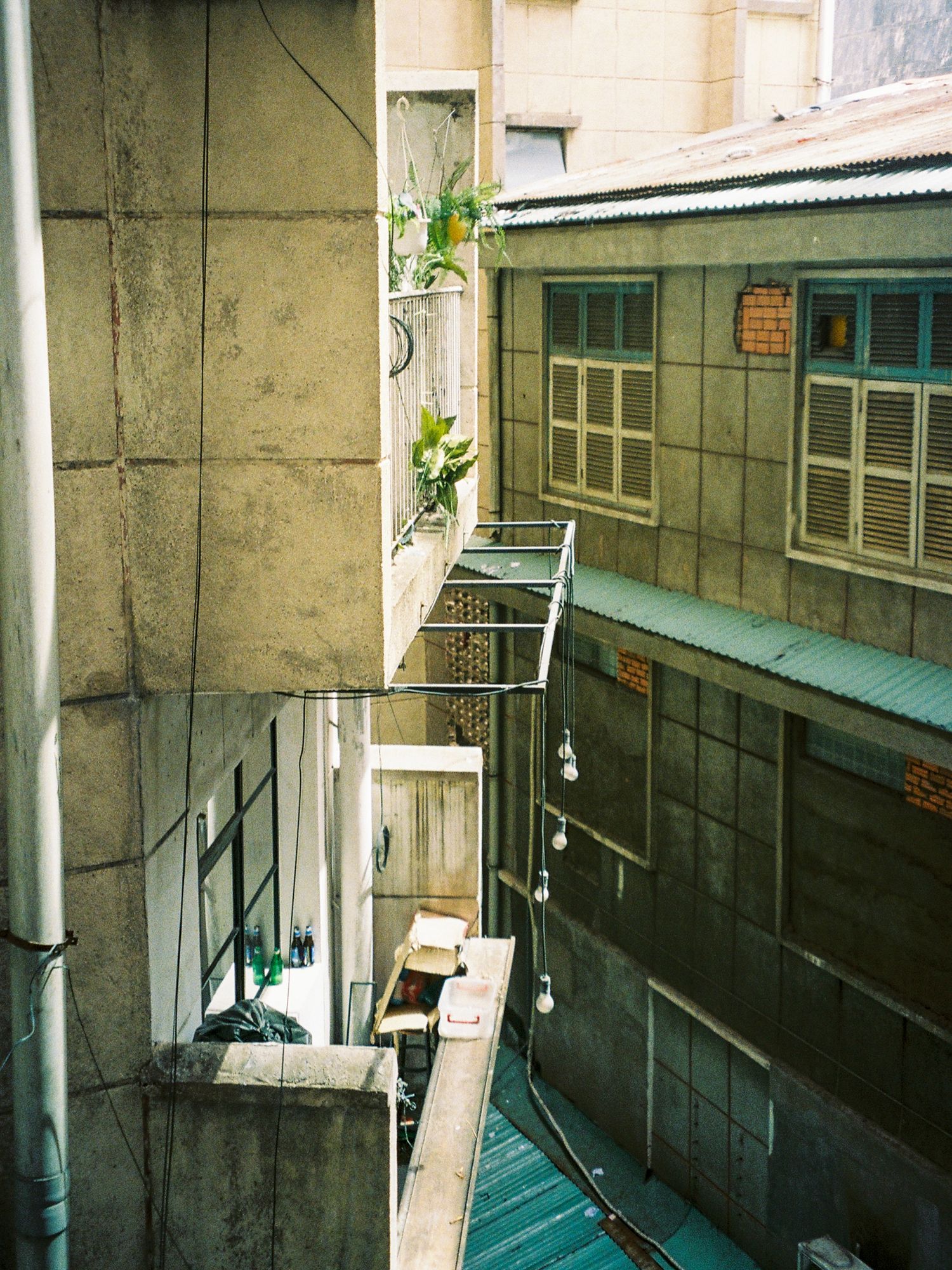 Urban alleyway with concrete walls and metal pipes leading to a turquoise-colored structure in the background.