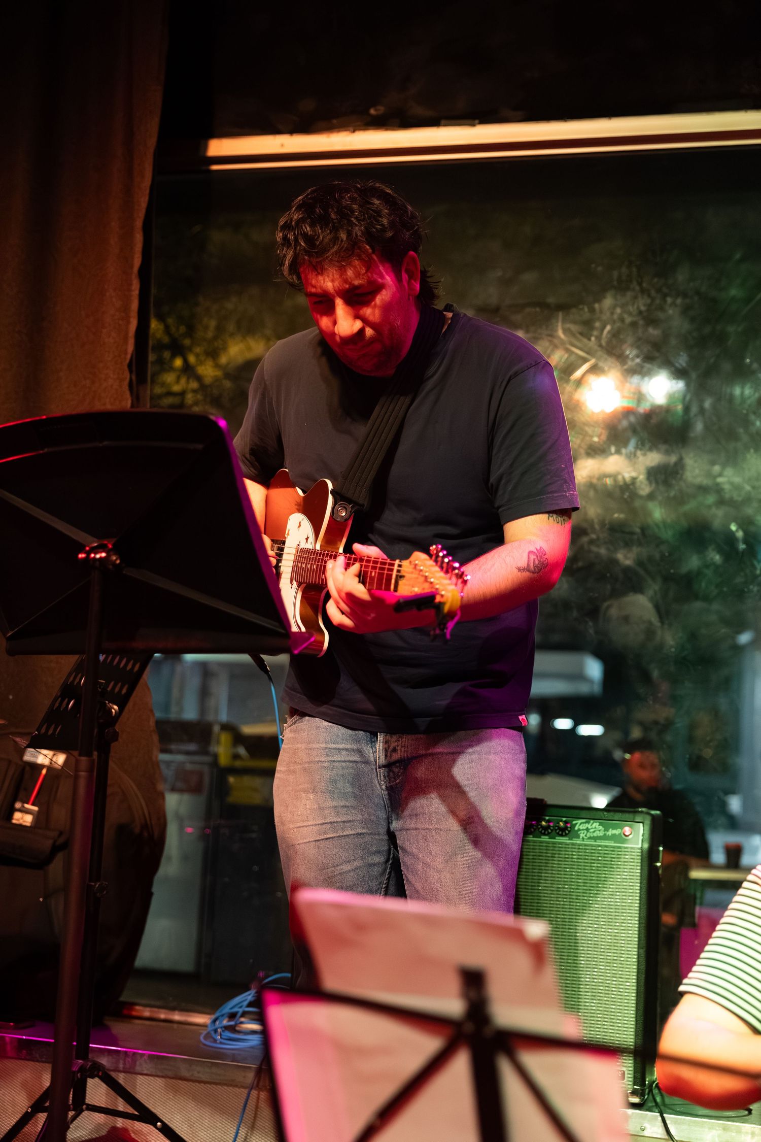 A musician performs on stage in dim lighting with pink and purple hues illuminating the performance space.