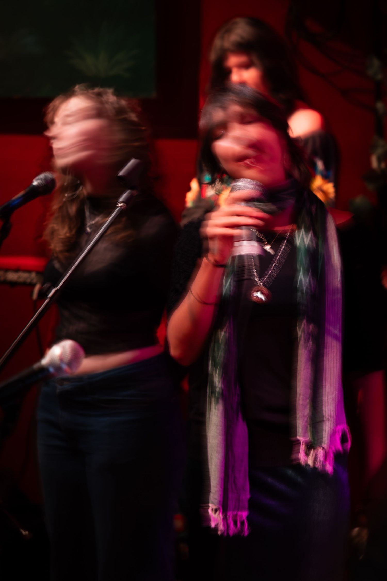 Motion blur captures performers singing into microphones on a dimly lit stage with red lighting effects.