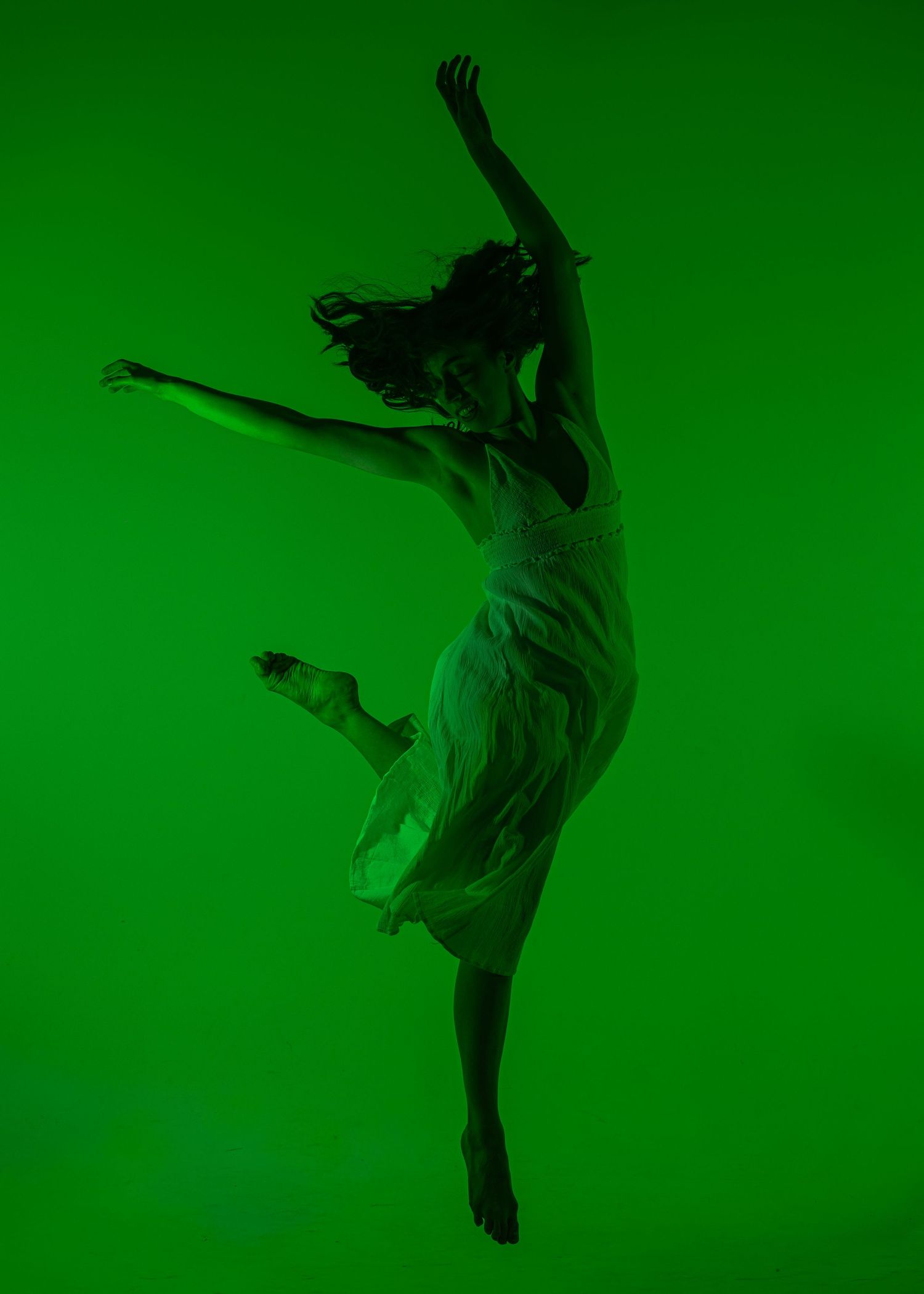 Dancer leaps gracefully in a white dress against a vibrant green background in a dynamic studio shot.