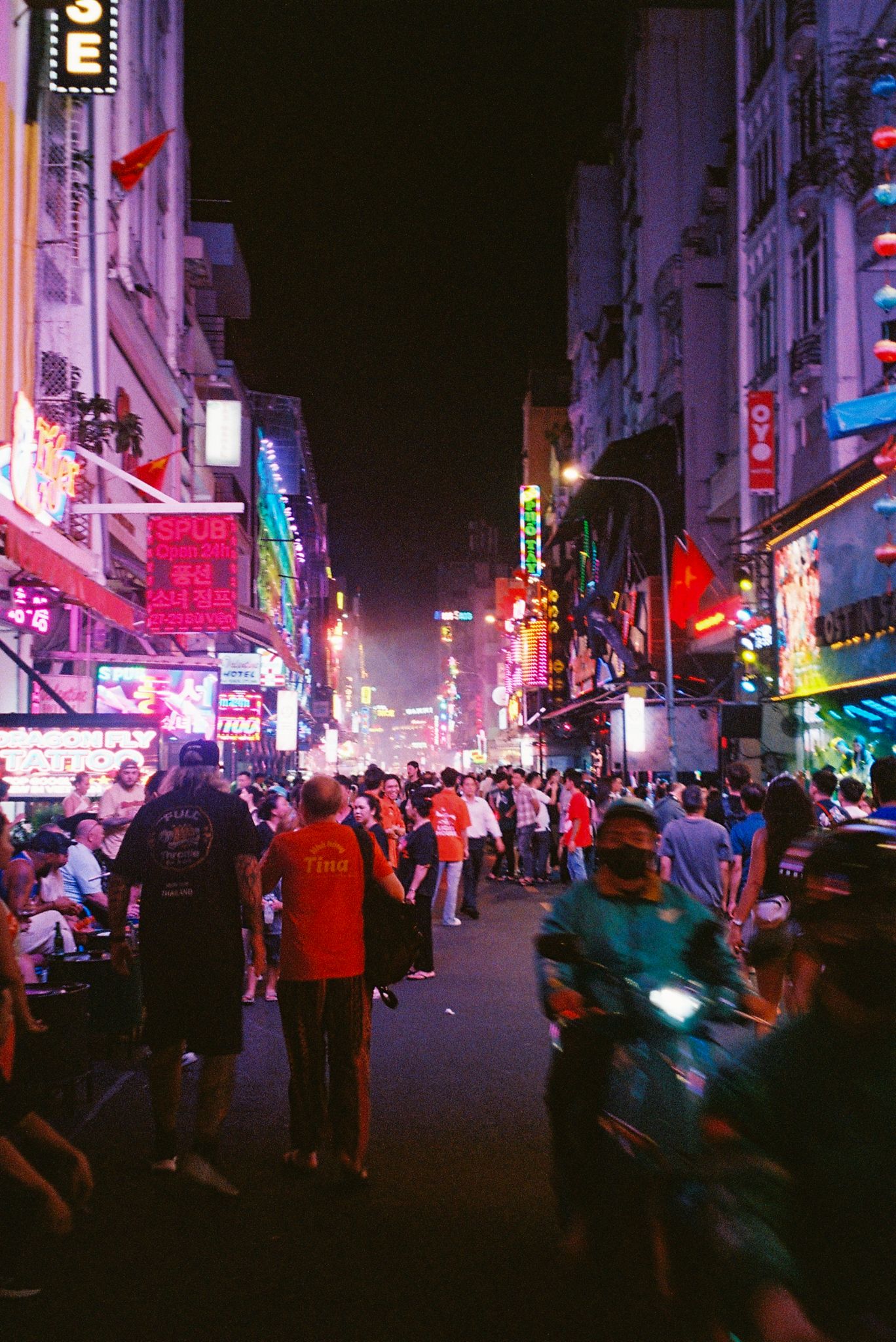 Vibrant neon-lit urban street scene at night with bustling crowds and colorful signage in Asian city.