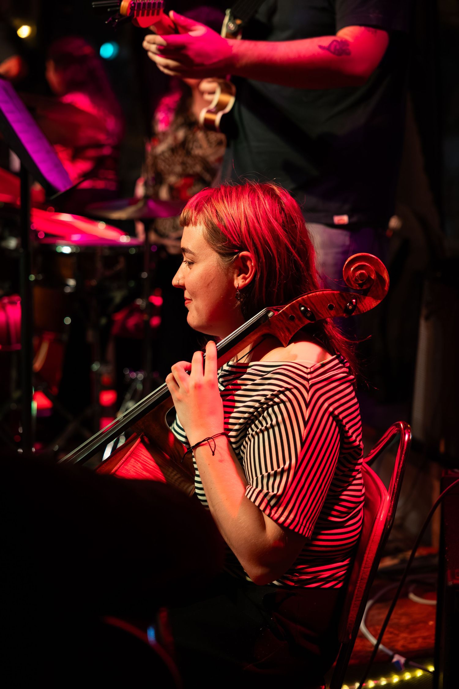 Performer in striped shirt illuminated by dramatic red stage lighting during a live music show.
