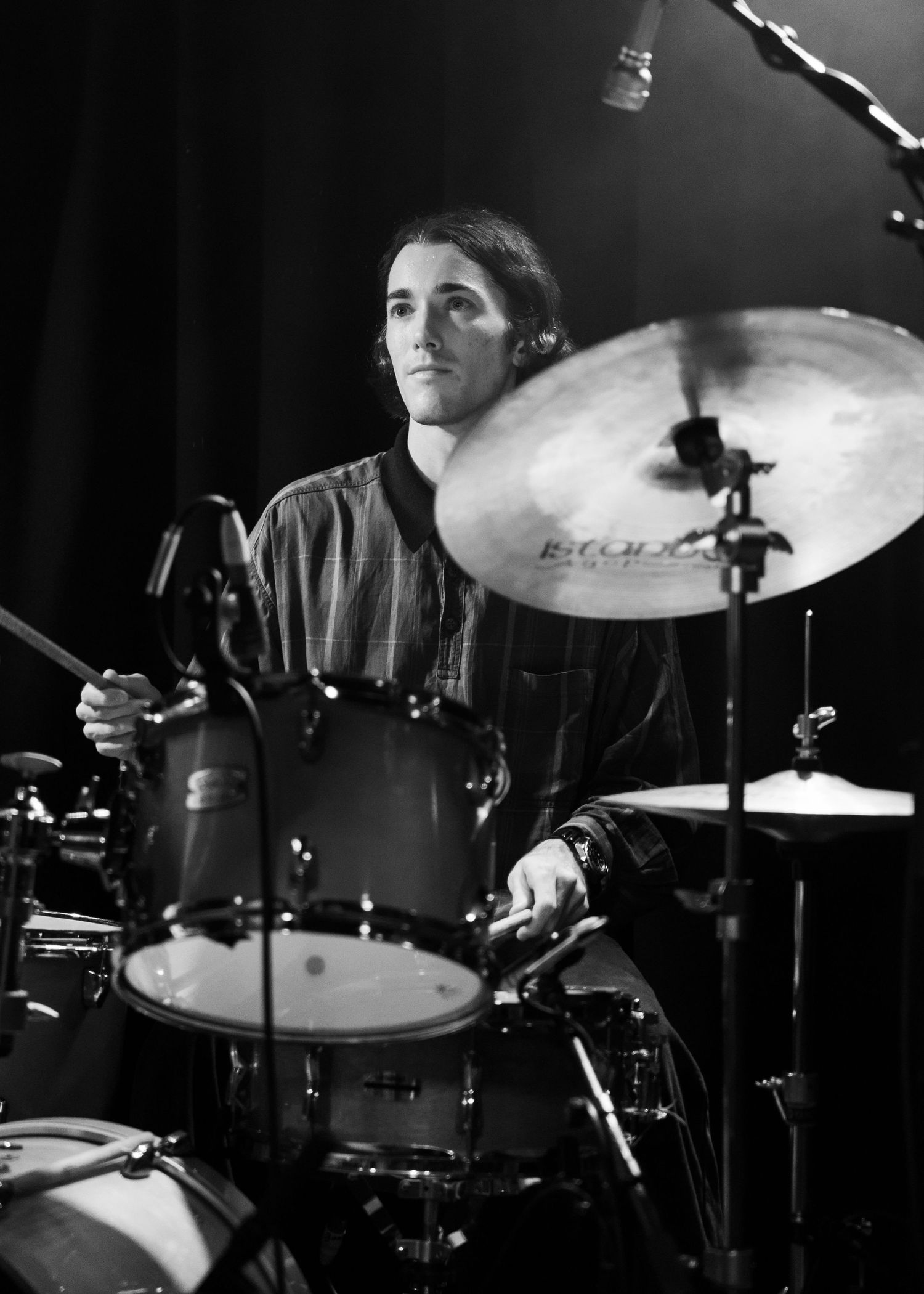Drummer playing a drum kit on stage captured in black and white during a live music performance.