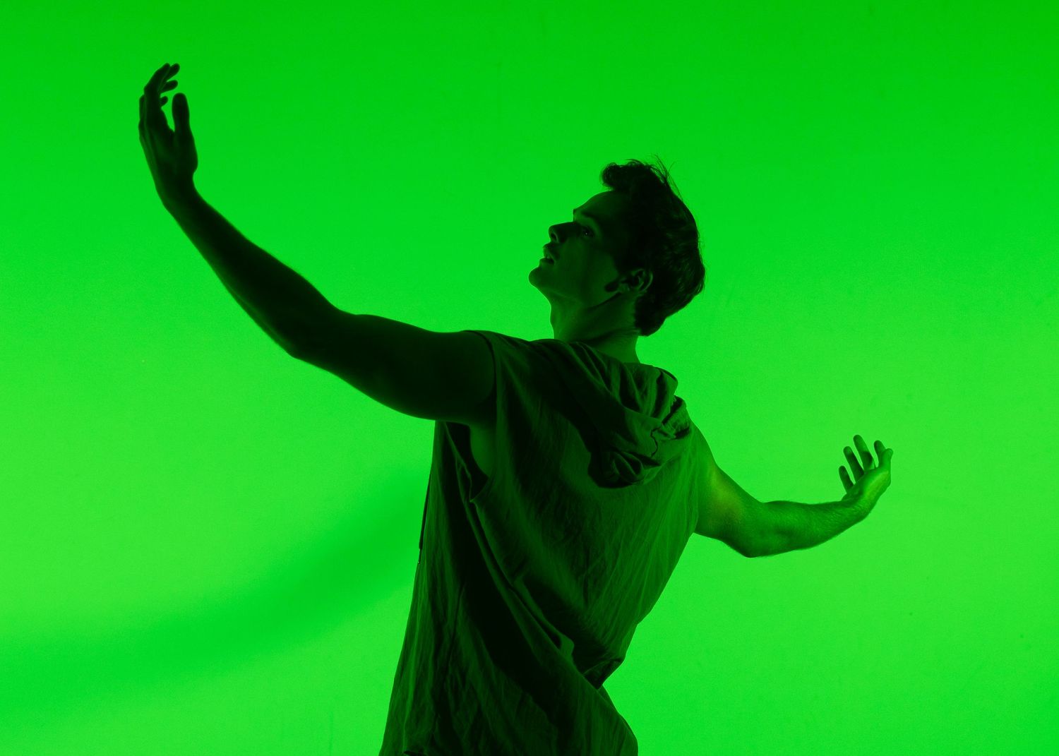 Dancer poses dramatically against a vibrant green background, reaching one arm upward in an expressive movement.