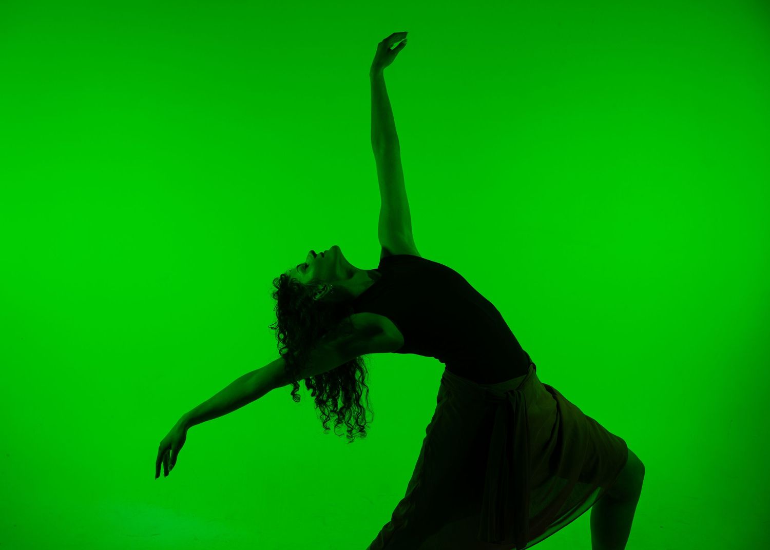 Silhouette of a female dancer striking a dramatic pose against a vibrant green background.