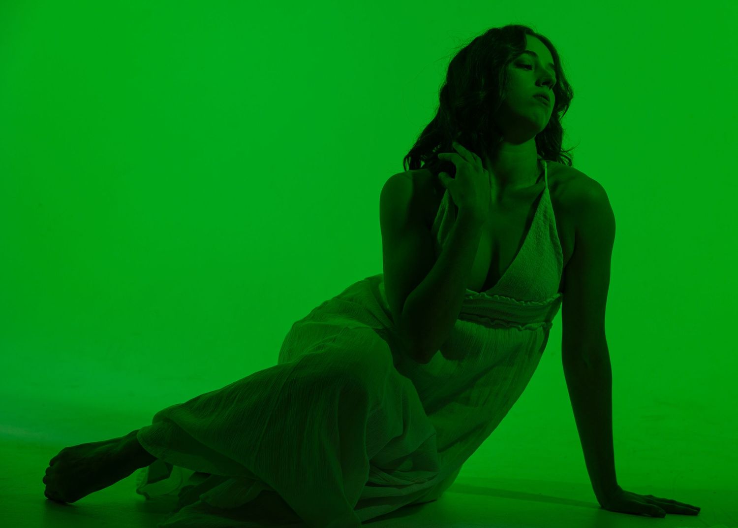 Woman in white dress poses gracefully against vibrant green background in artistic studio photography.