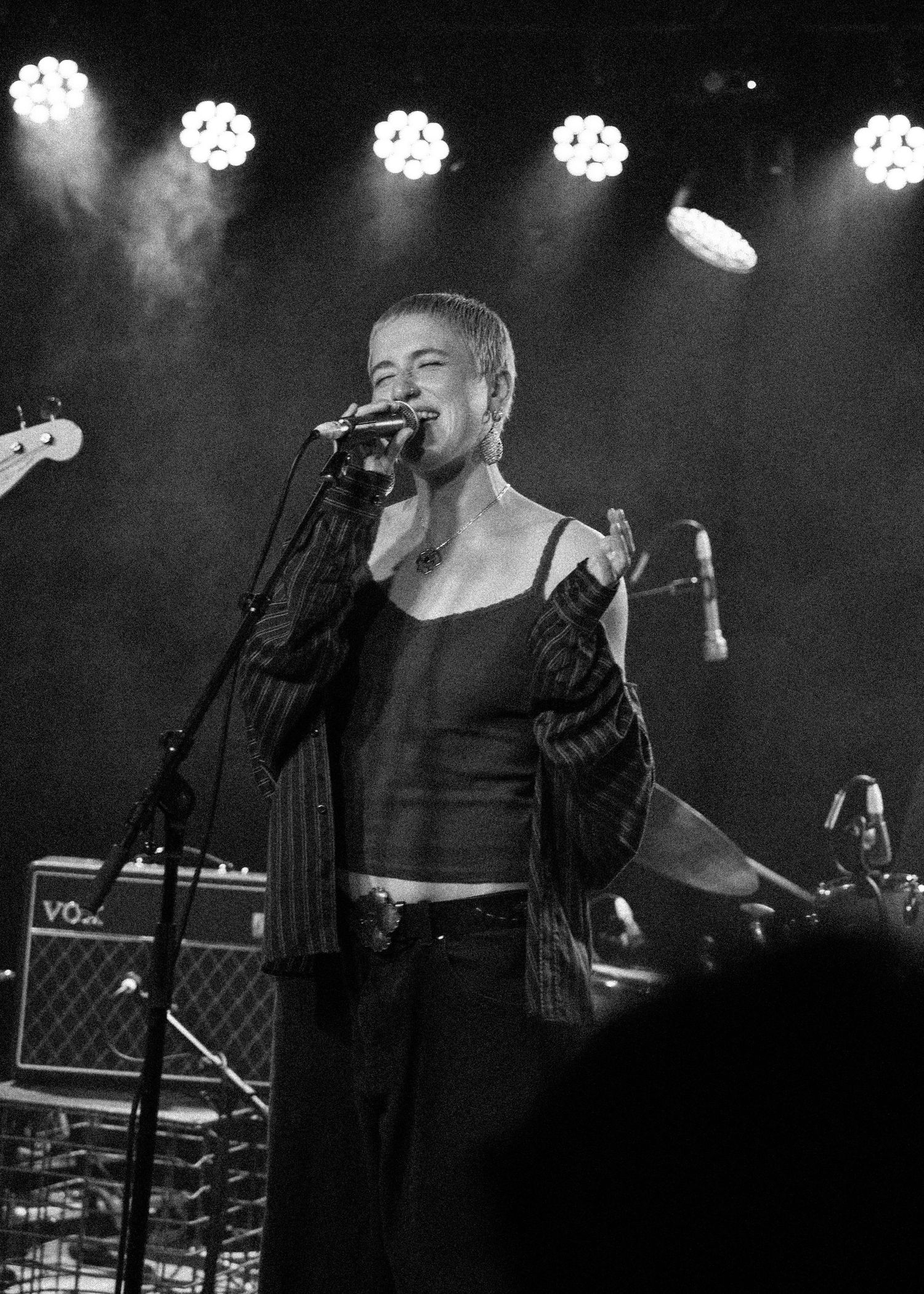 Black and white photo of a female singer performing on stage with microphone under bright stage lights.