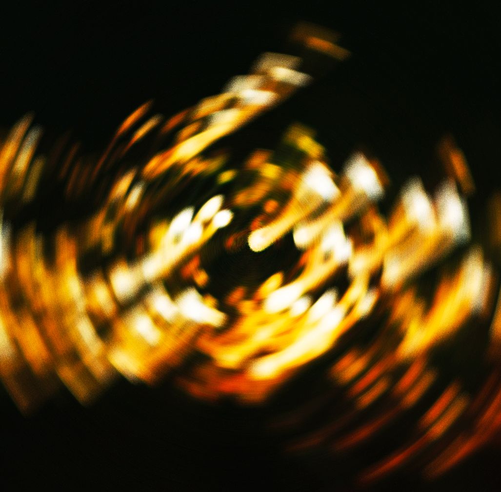 Abstract swirling golden light bokeh creating a hypnotic spiral vortex pattern against a dark black background.