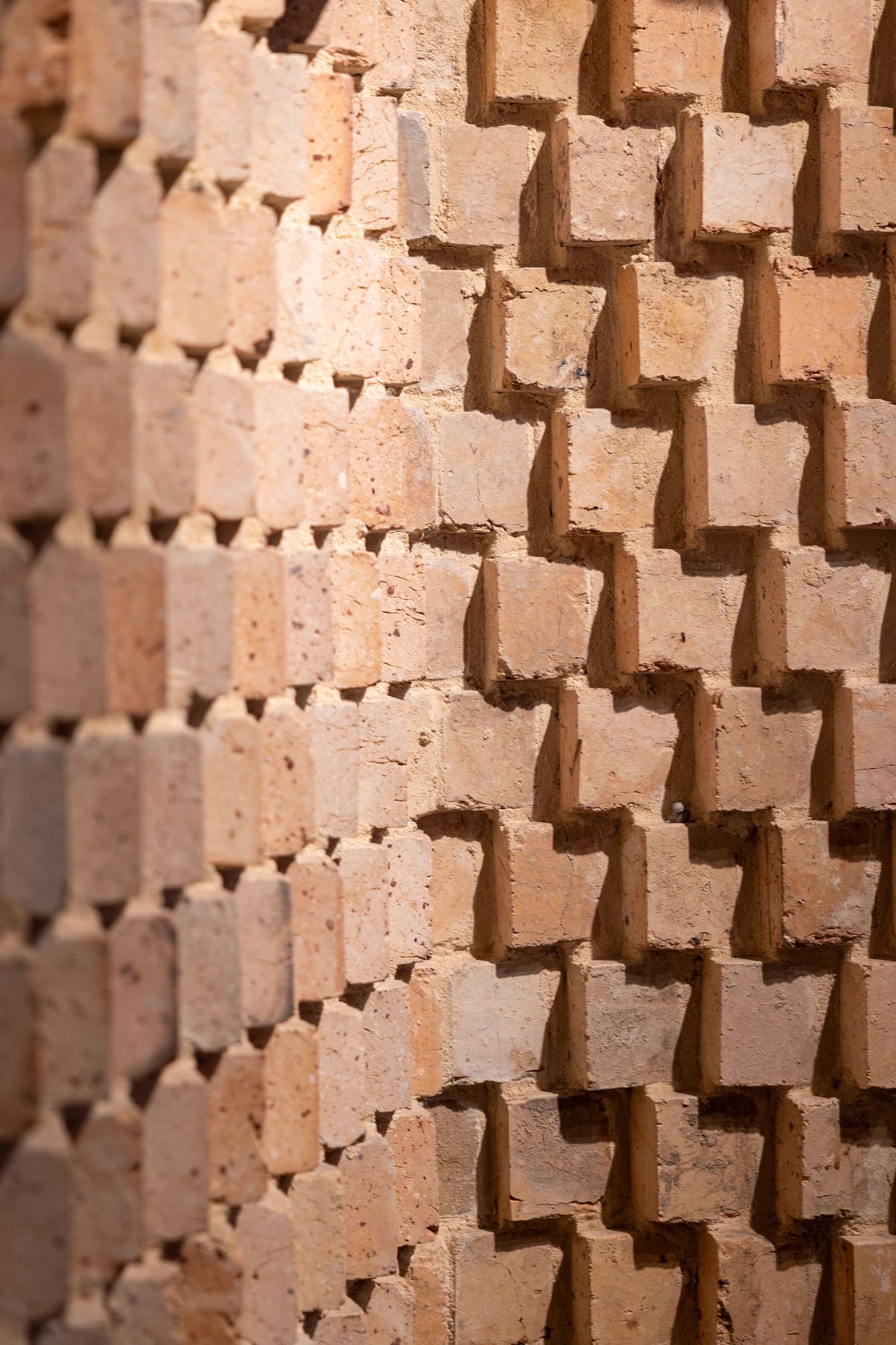 Close-up of a decorative terracotta brick wall with alternating protruding blocks creating a geometric shadow pattern.