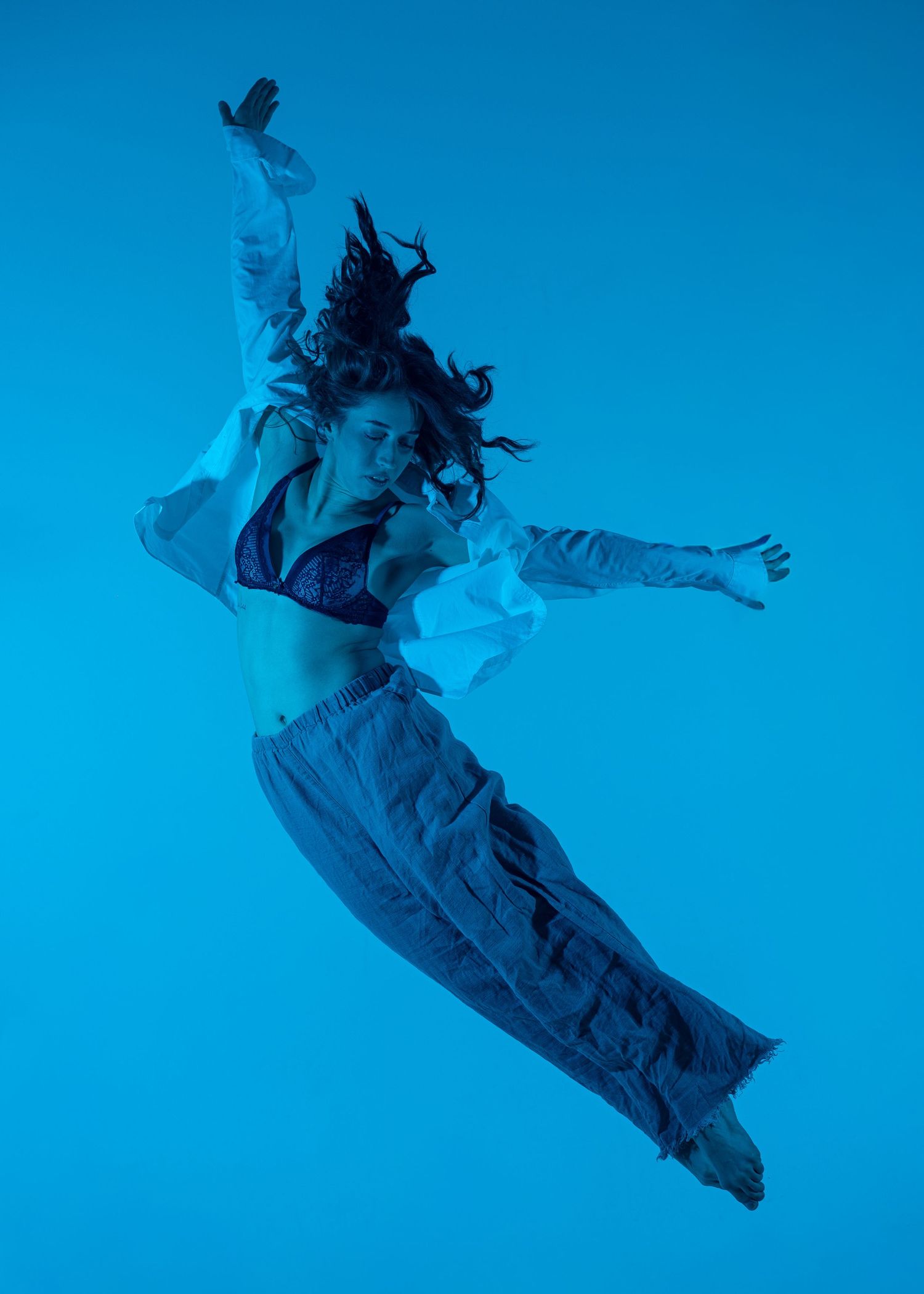 Woman leaping dynamically against a vivid blue background wearing wide-leg pants and a white shirt.