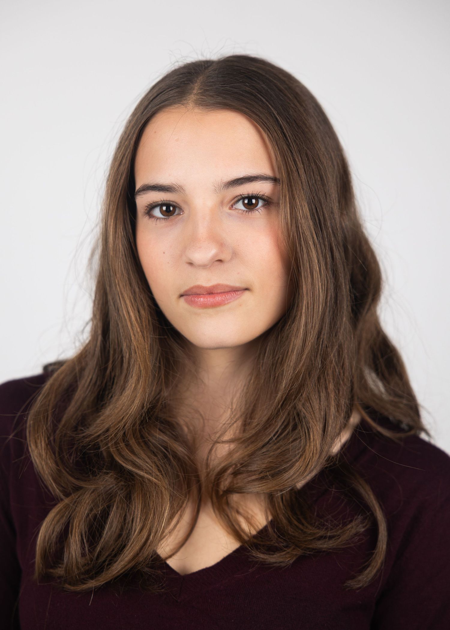 Young woman with long brown hair wearing a dark maroon top poses for a professional headshot portrait.