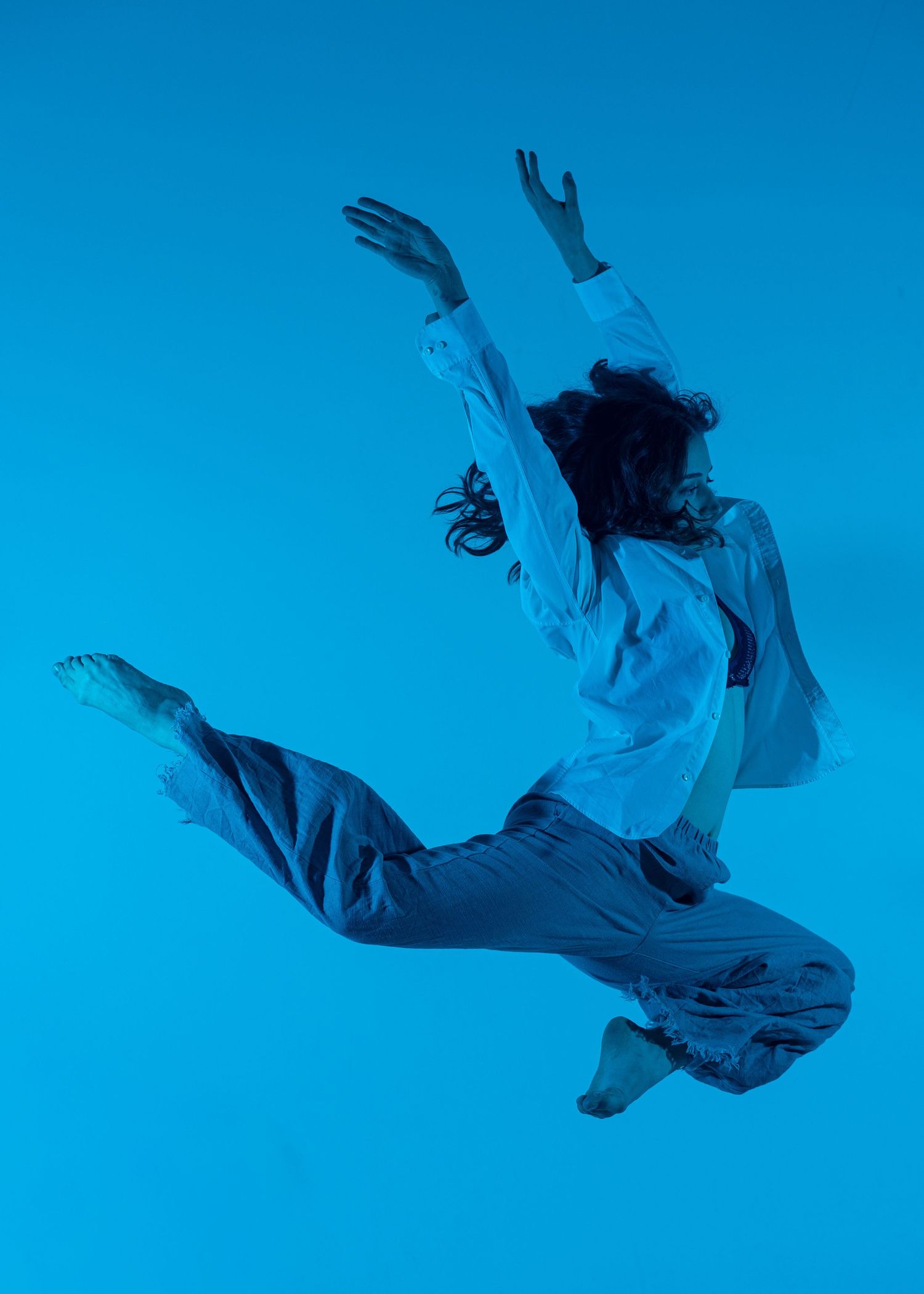 A dancer leaps dynamically in white outfit against a vivid blue background.