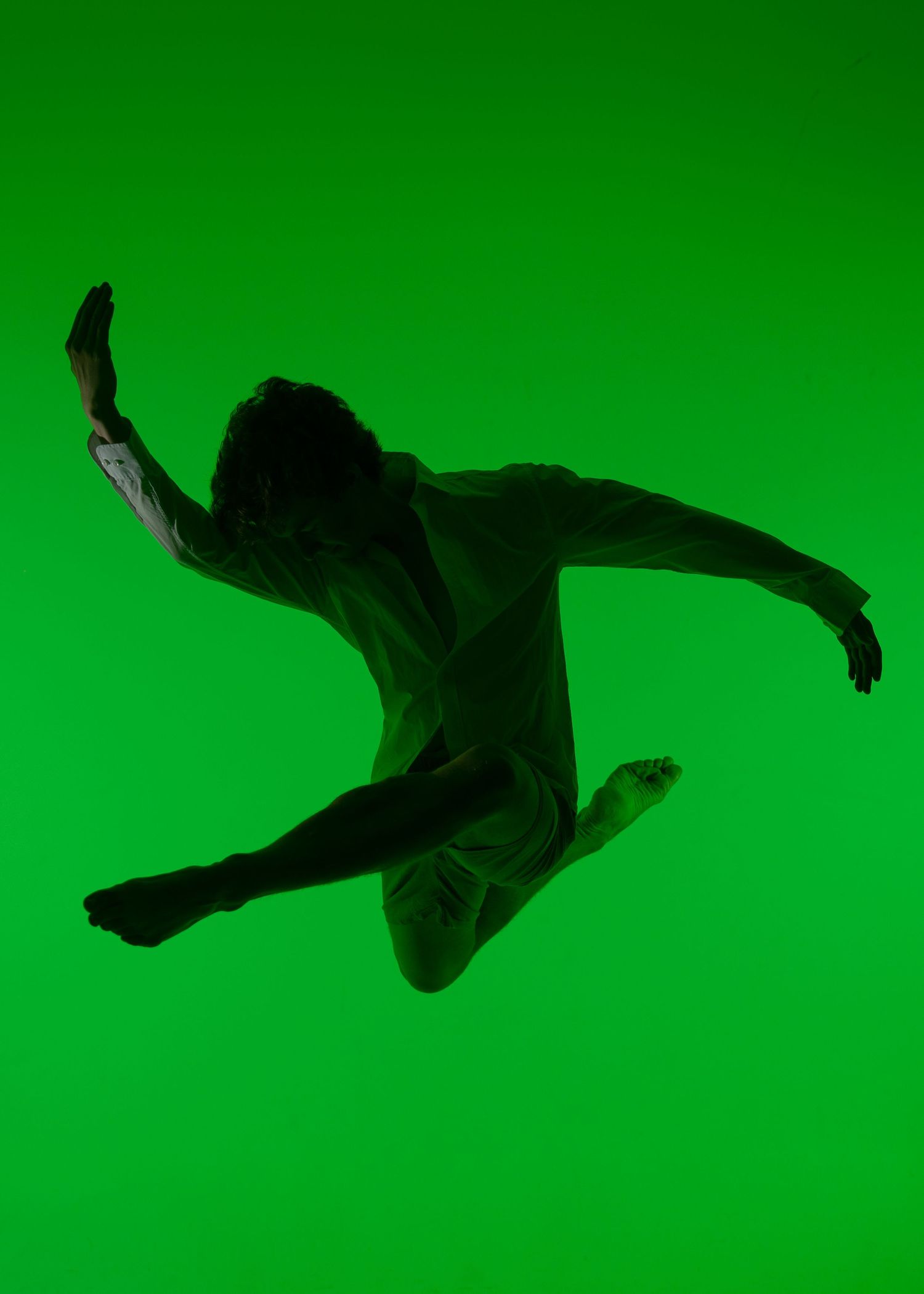 Silhouetted dancer leaps dynamically against a vibrant green background in an artistic performance photo.