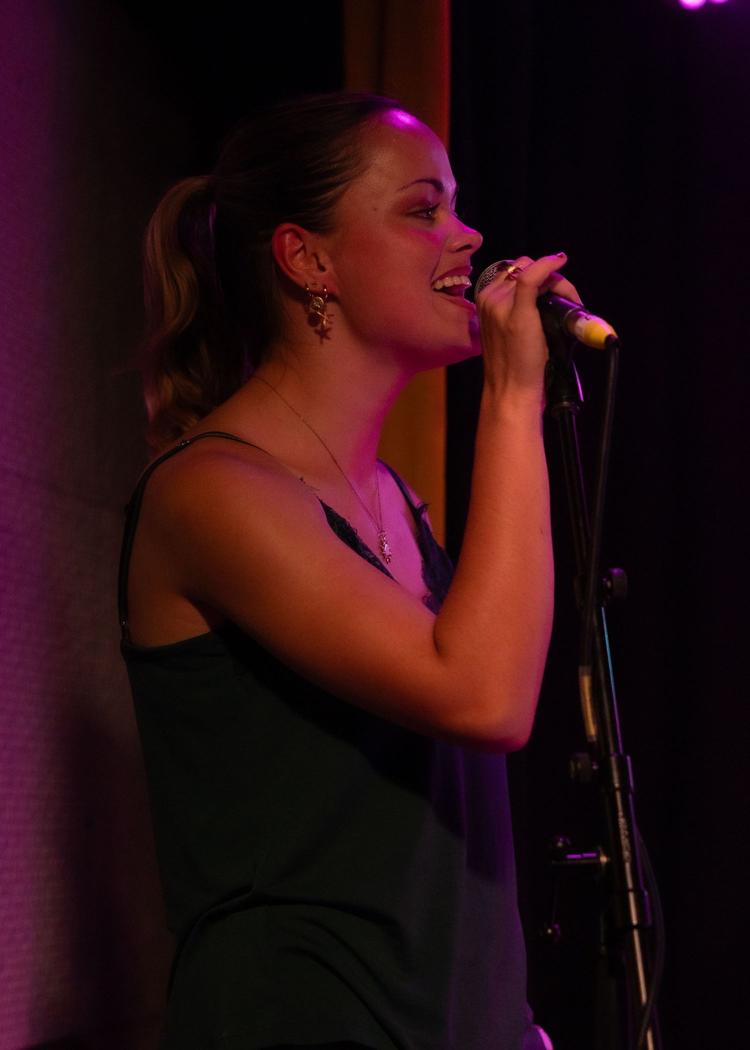 Woman in green dress singing into microphone on stage under pink and purple stage lighting.