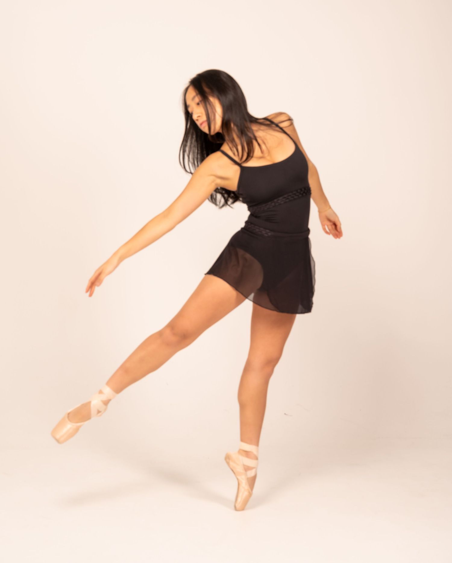 Graceful ballet dancer in black leotard performs dynamic movements against white background.