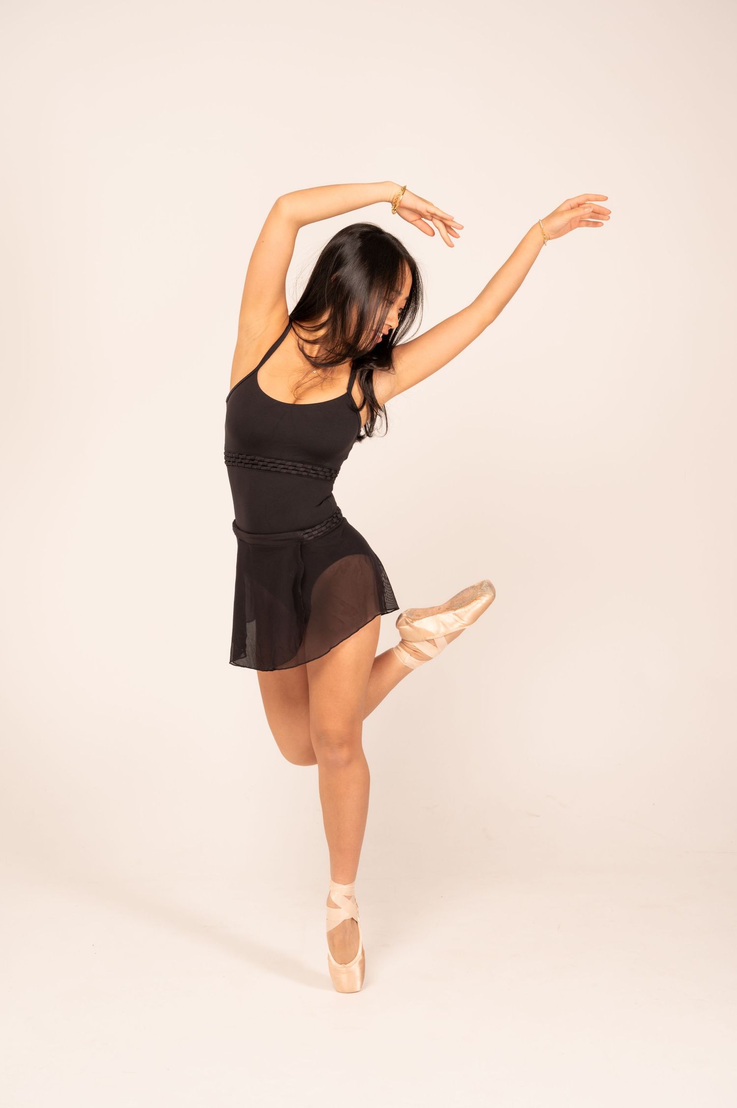 Ballet dancer in black leotard and tutu performs graceful poses against white background.