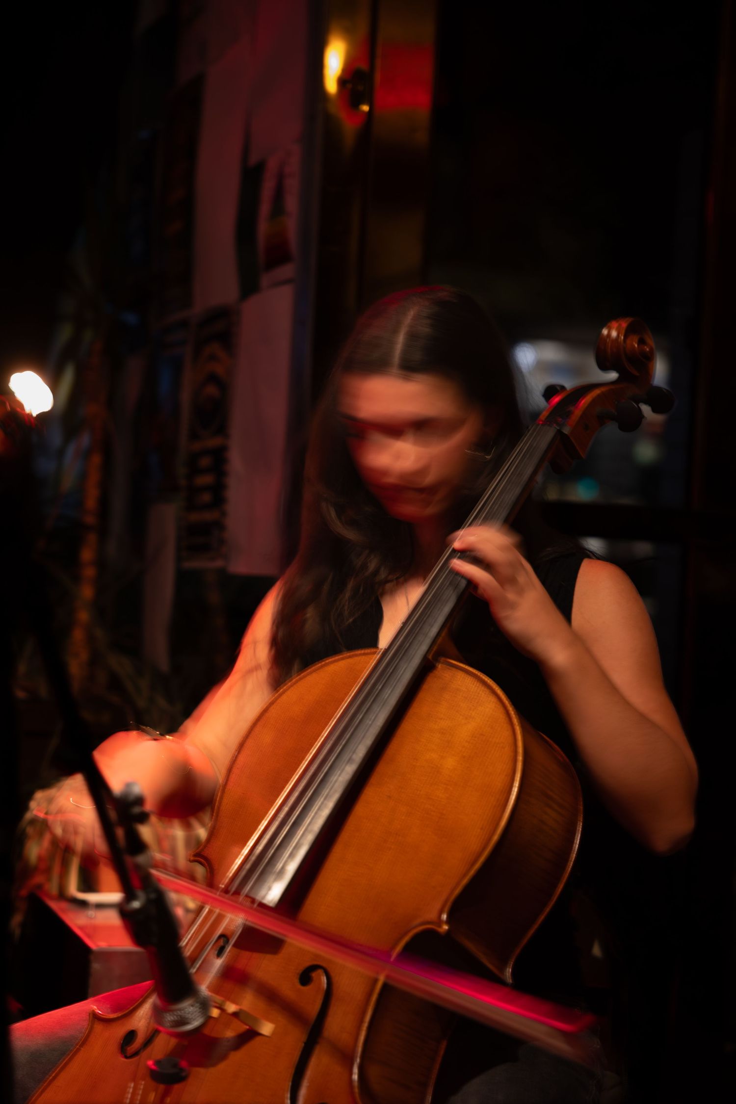 Close-up of cello being played with bow in moody red stage lighting during musical performance.