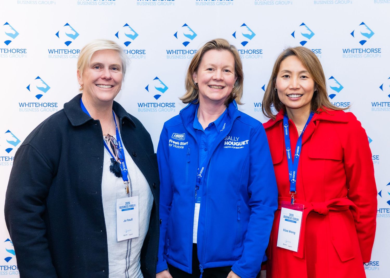 Three women smiling together in front of a Whitehorse branded backdrop at a professional event.