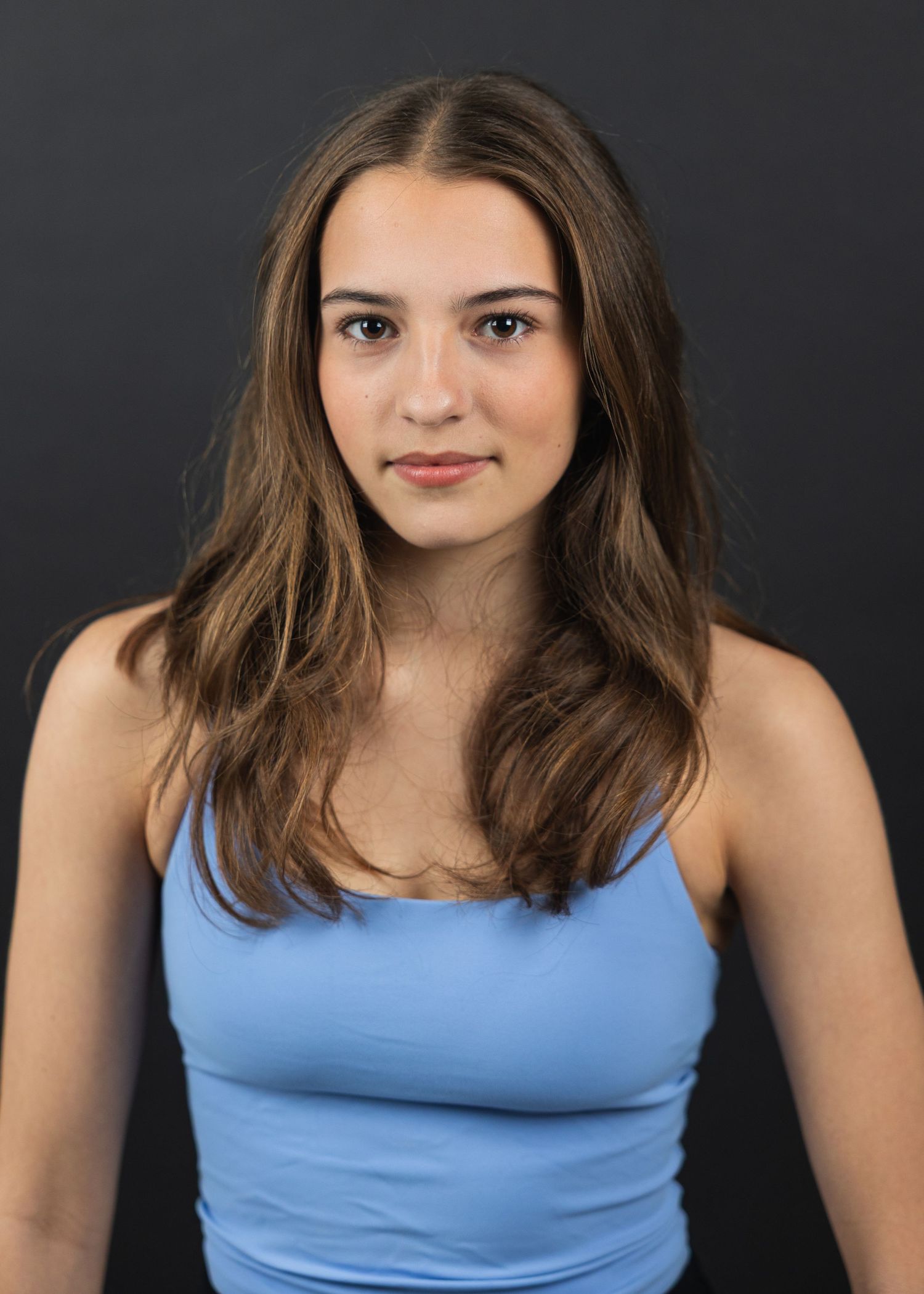 Young woman with brown hair wearing a light blue tank top poses for a professional headshot photo.