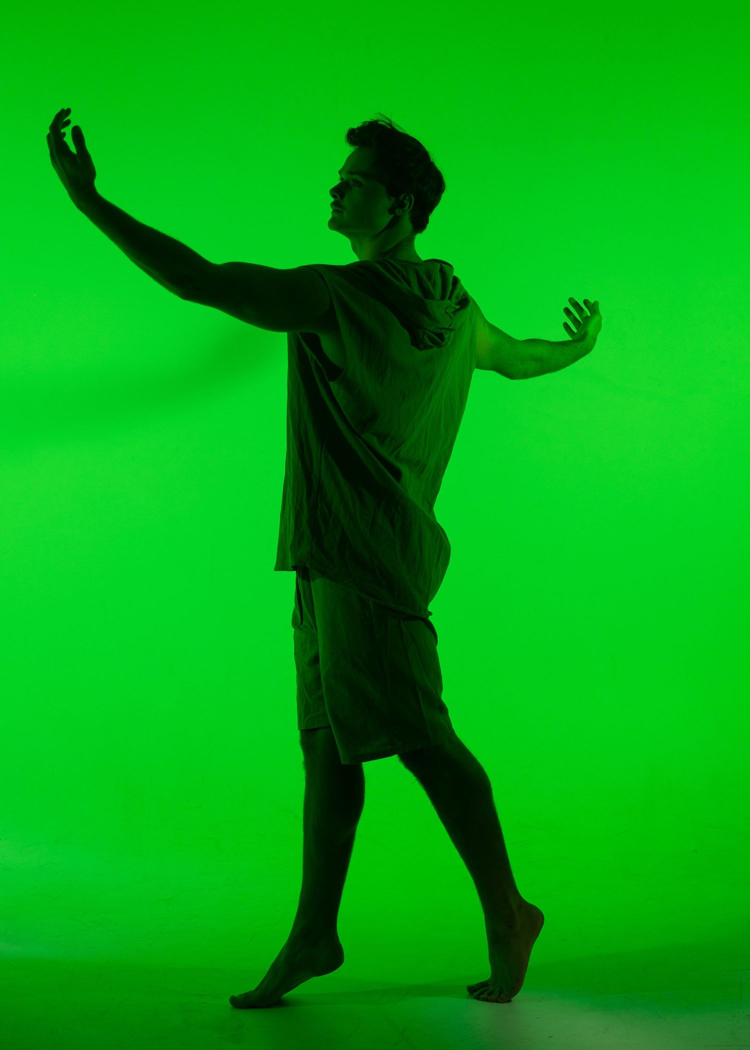 Male dancer in t-shirt and shorts performs expressive contemporary dance in green light.