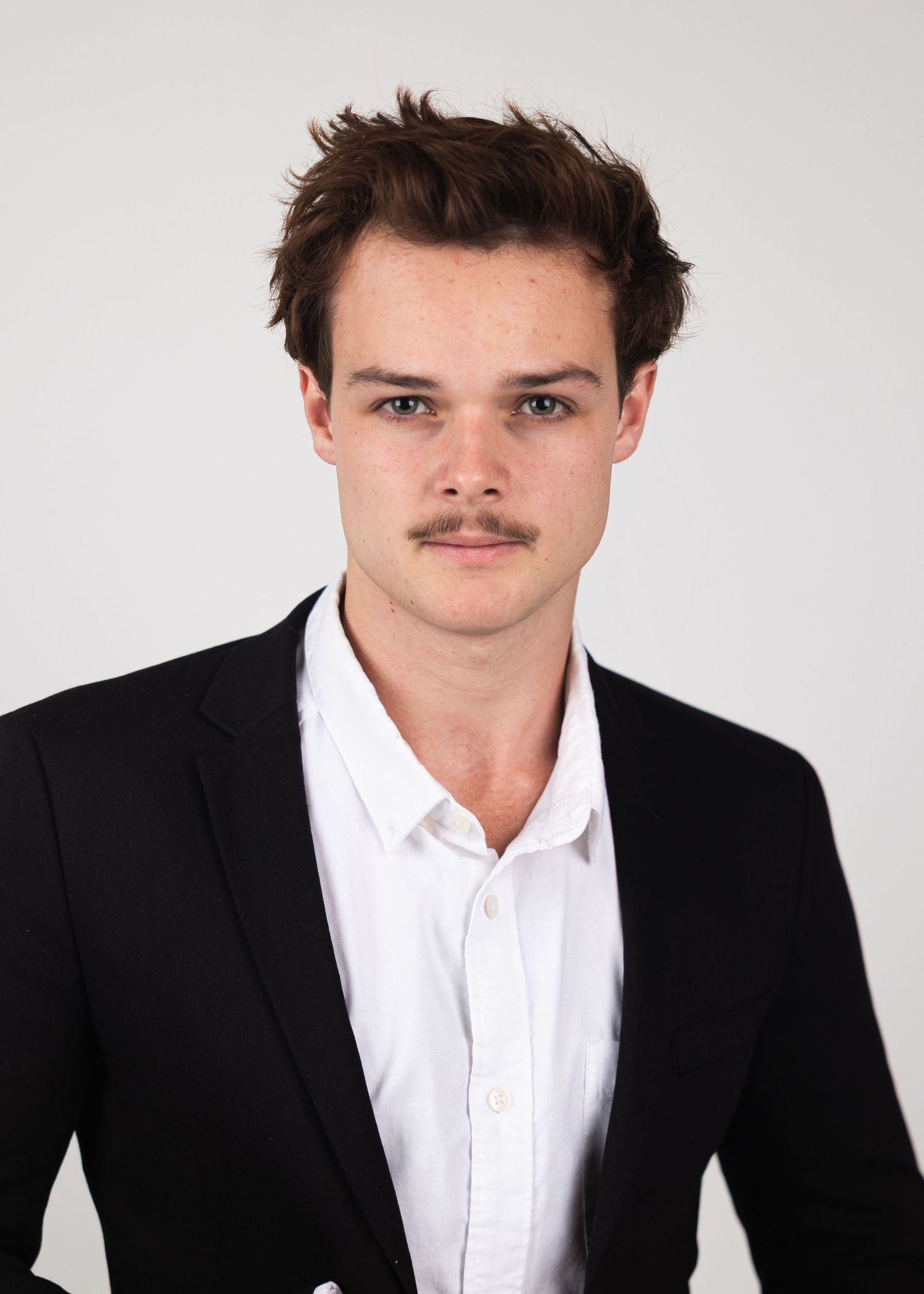 Young man with mustache in black blazer poses for serious professional portrait headshot.