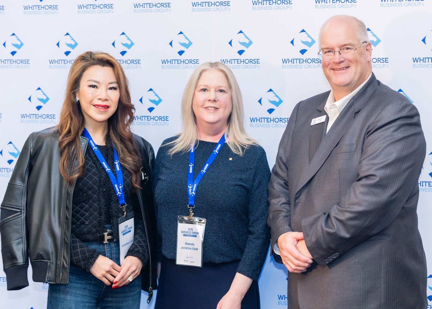 Three professionals pose smiling in front of a Whitehorse branded backdrop at a corporate event.