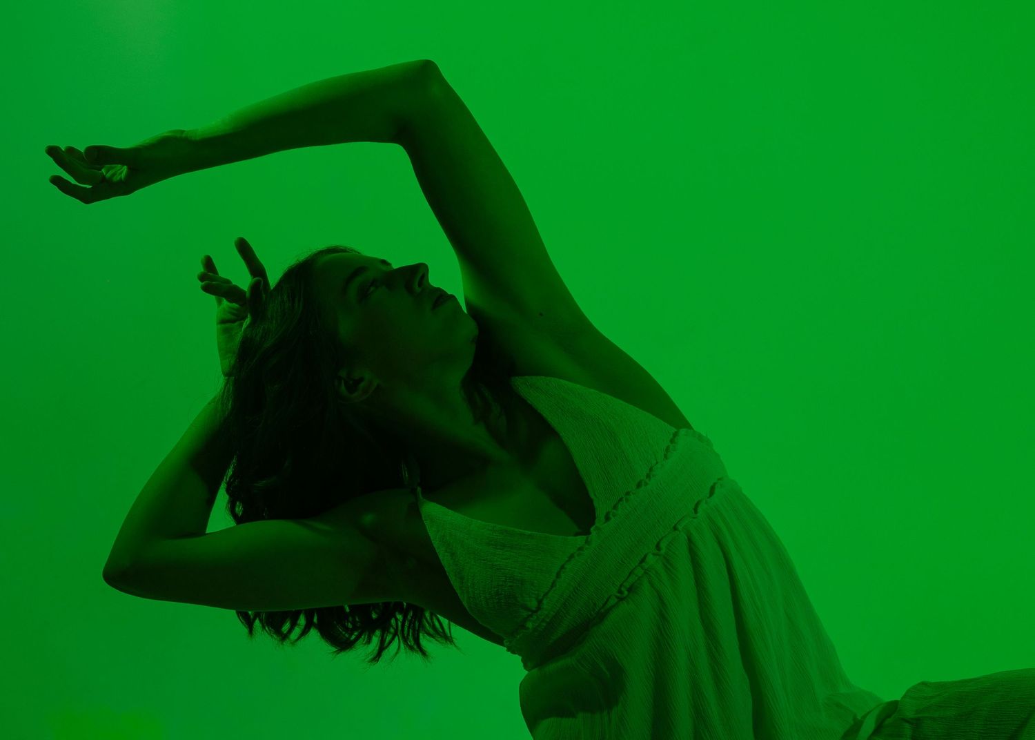 A dancer poses gracefully against a vibrant green background, arching her body with one arm raised overhead.
