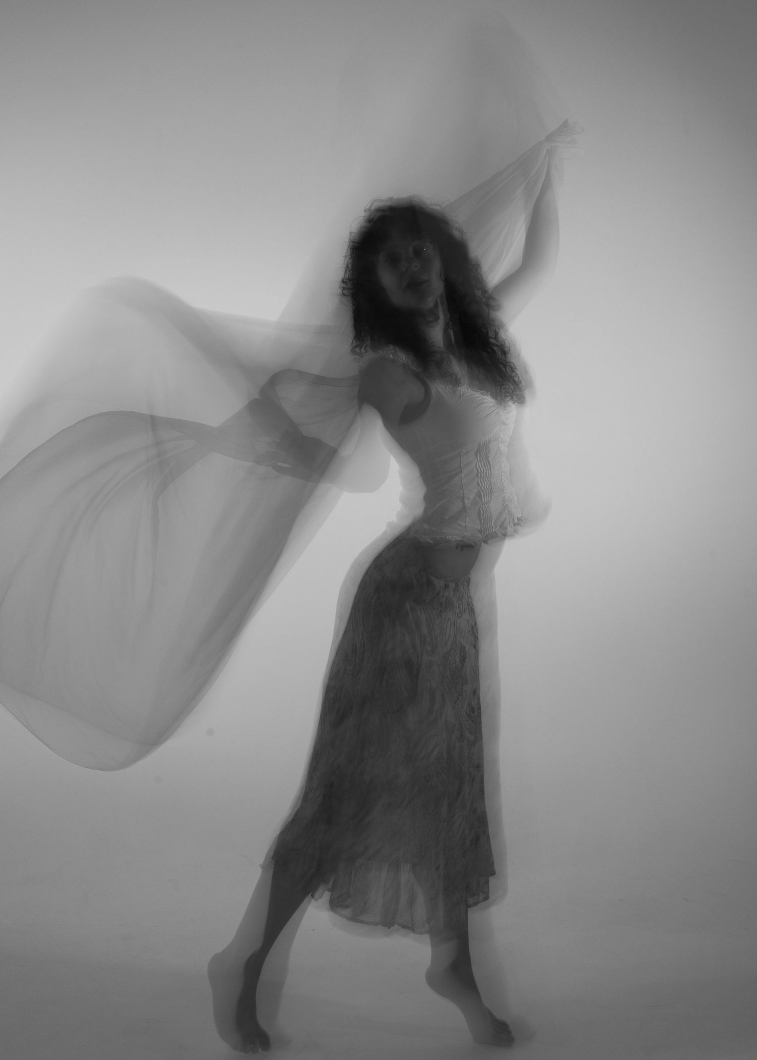 Artistic black and white long-exposure photo of a woman dancing with flowing sheer fabric.