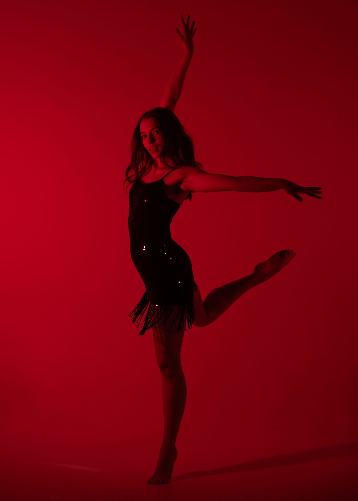 Female ballet dancer in a black sequined dress poses elegantly against a dramatic red background.