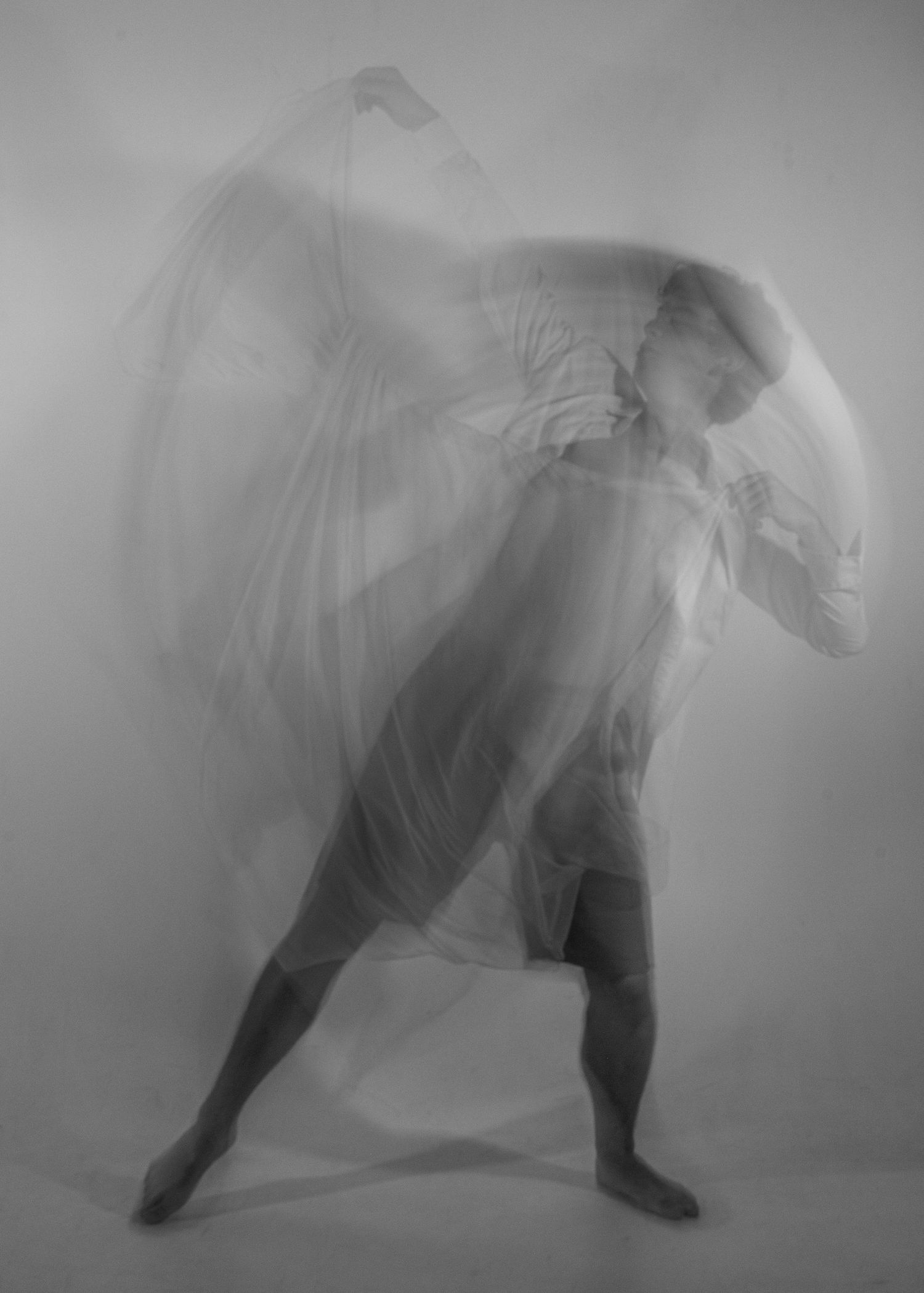 Black and white photo of a dancer wrapped in flowing sheer fabric mid-movement.