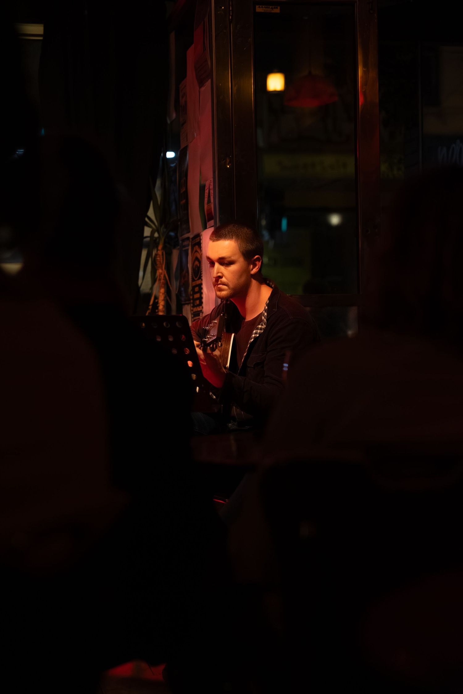 Musicians playing in a dark concert venue illuminated by moody red and green lighting.