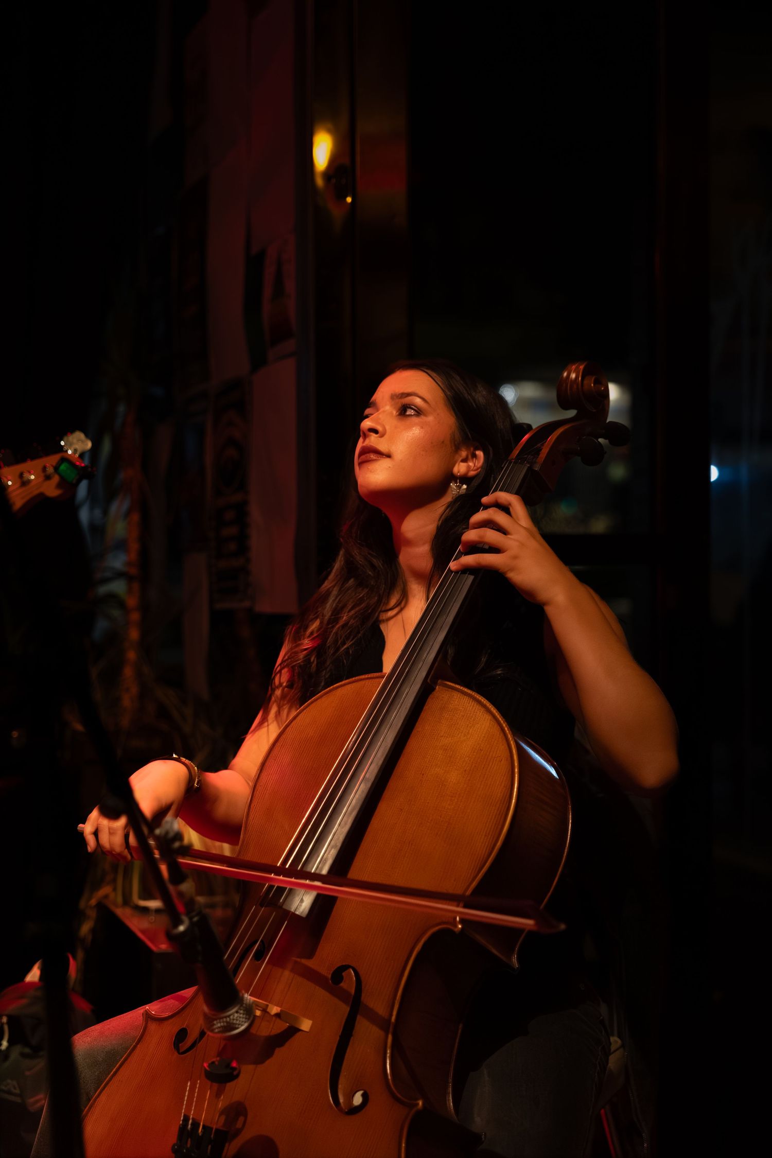 A musician performs on a cello in dramatic low lighting during an intimate concert setting.