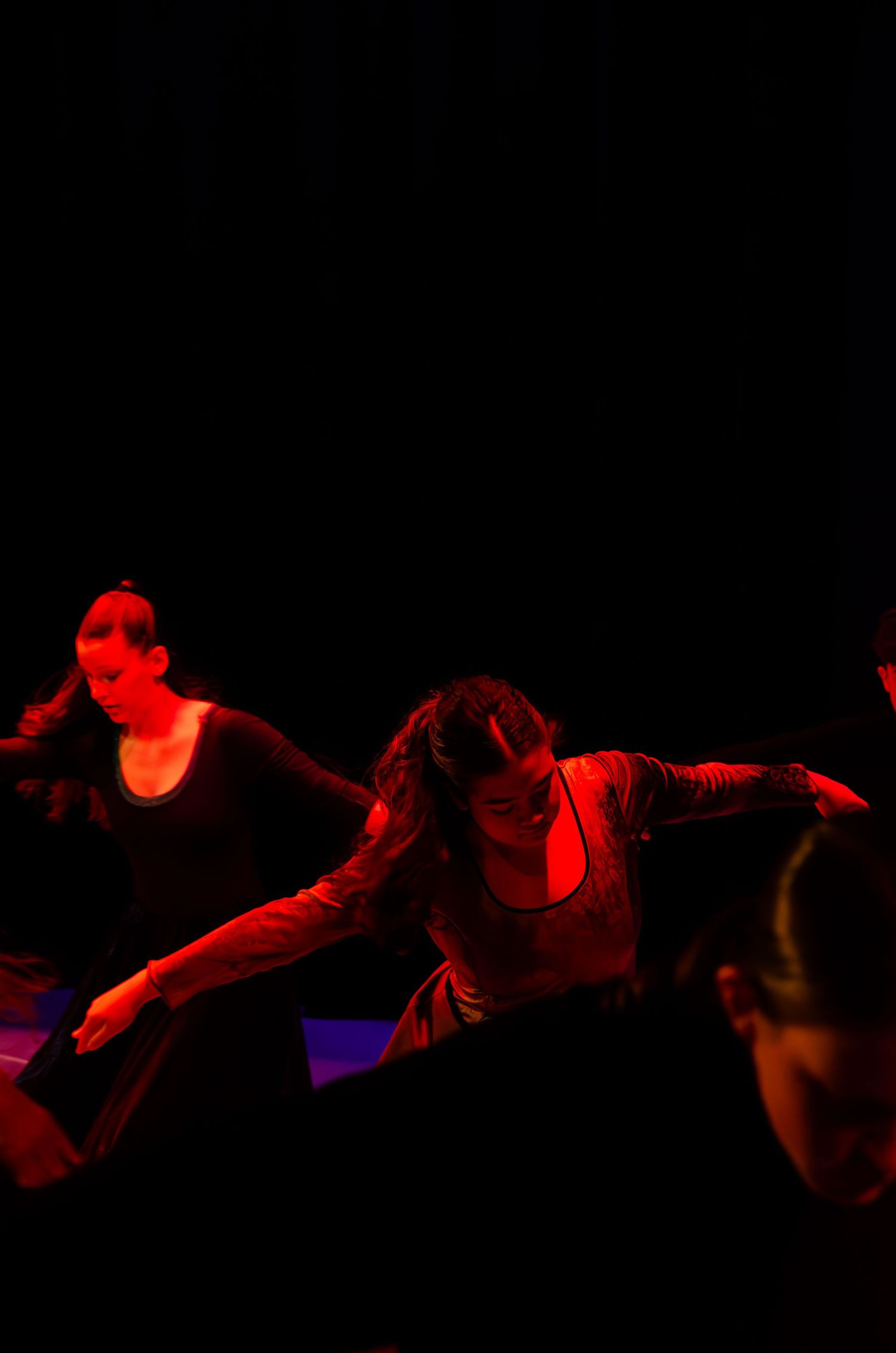 Dancers perform under dramatic red stage lighting in a contemporary dance performance on a dark stage.