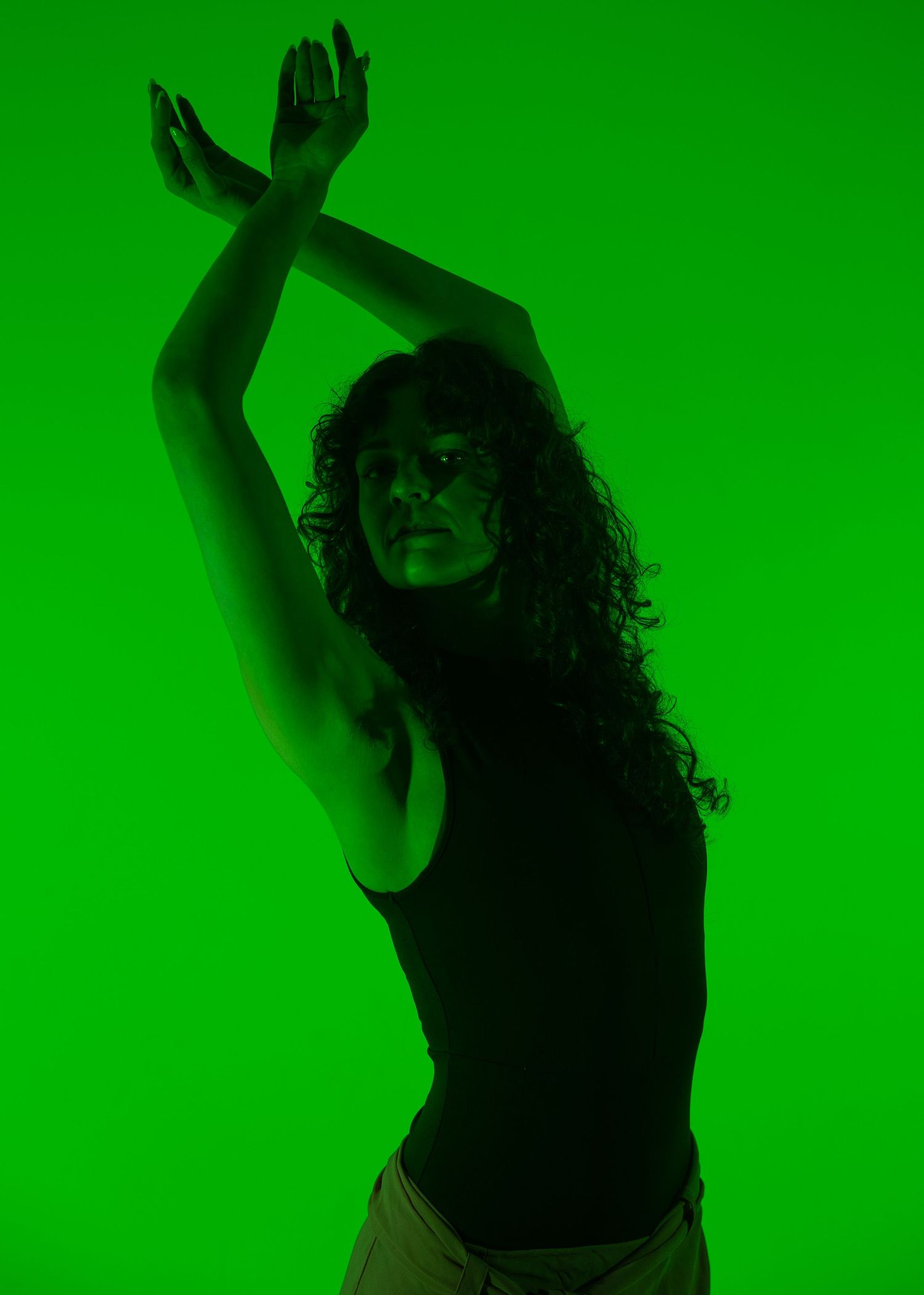 A woman with curly hair dances gracefully with arms raised under dramatic green lighting.
