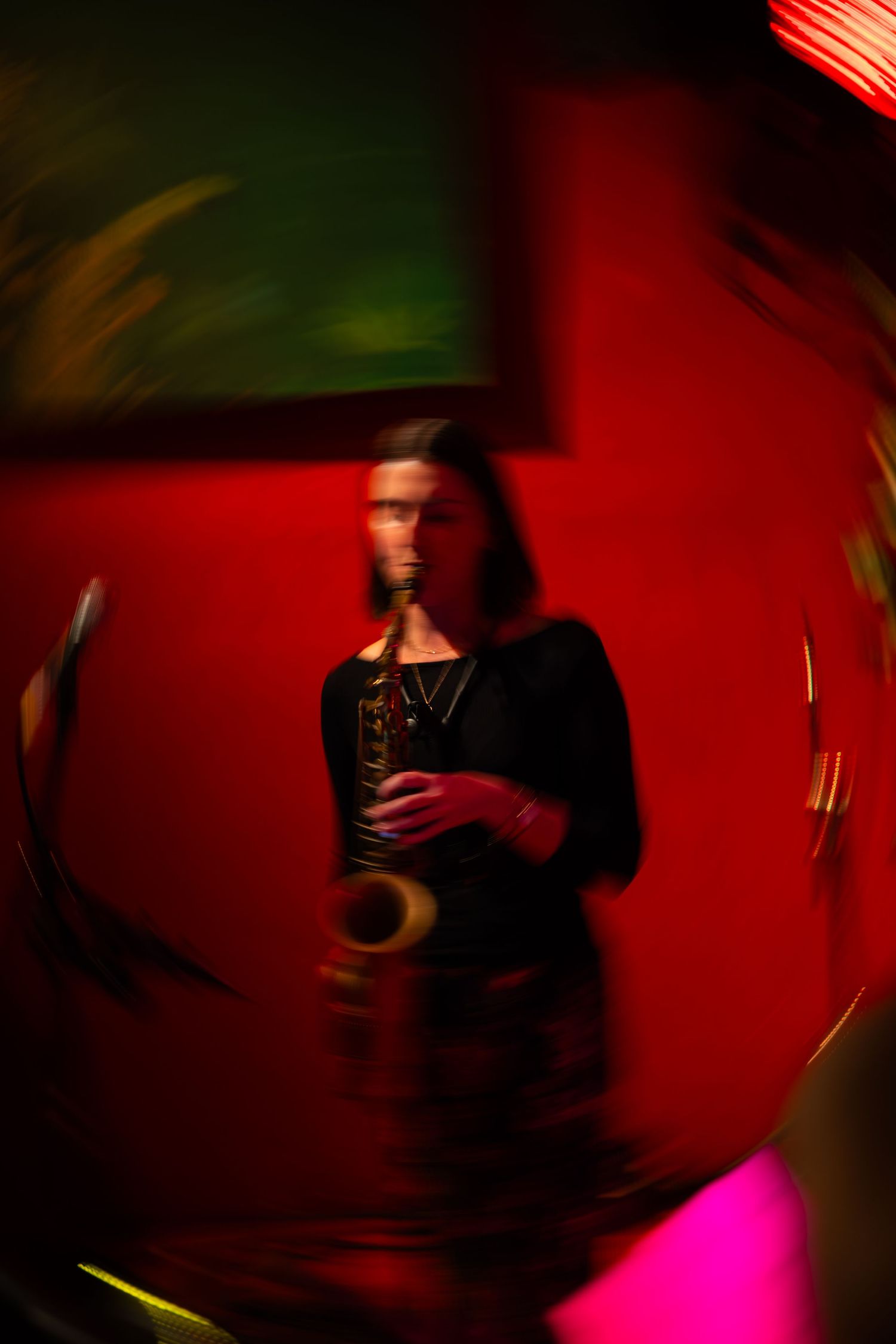 Saxophone player performing in a dimly lit venue with red and green ambient lighting creating a moody atmosphere.