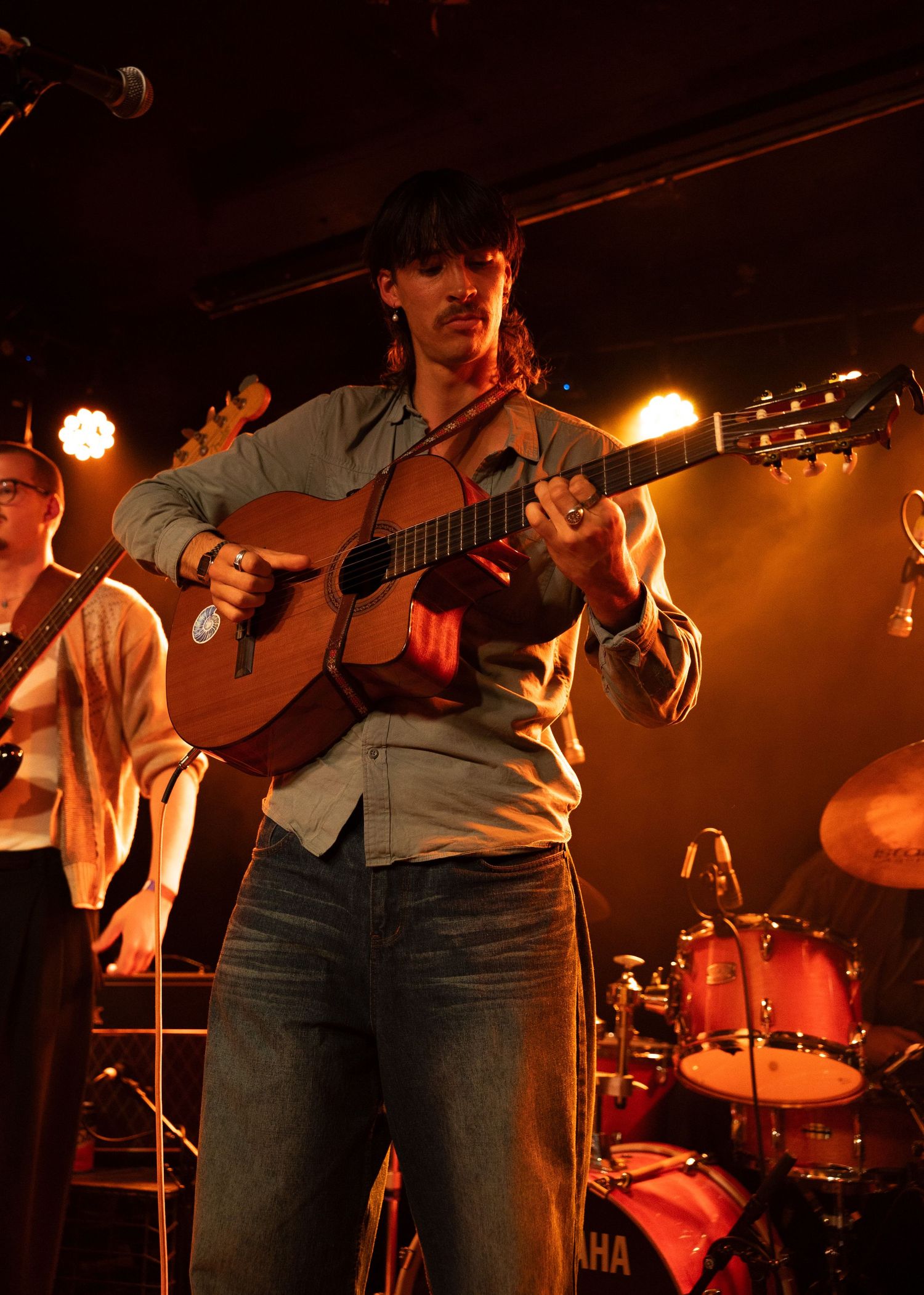 Musician playing acoustic guitar on stage under warm amber stage lights during a live performance.