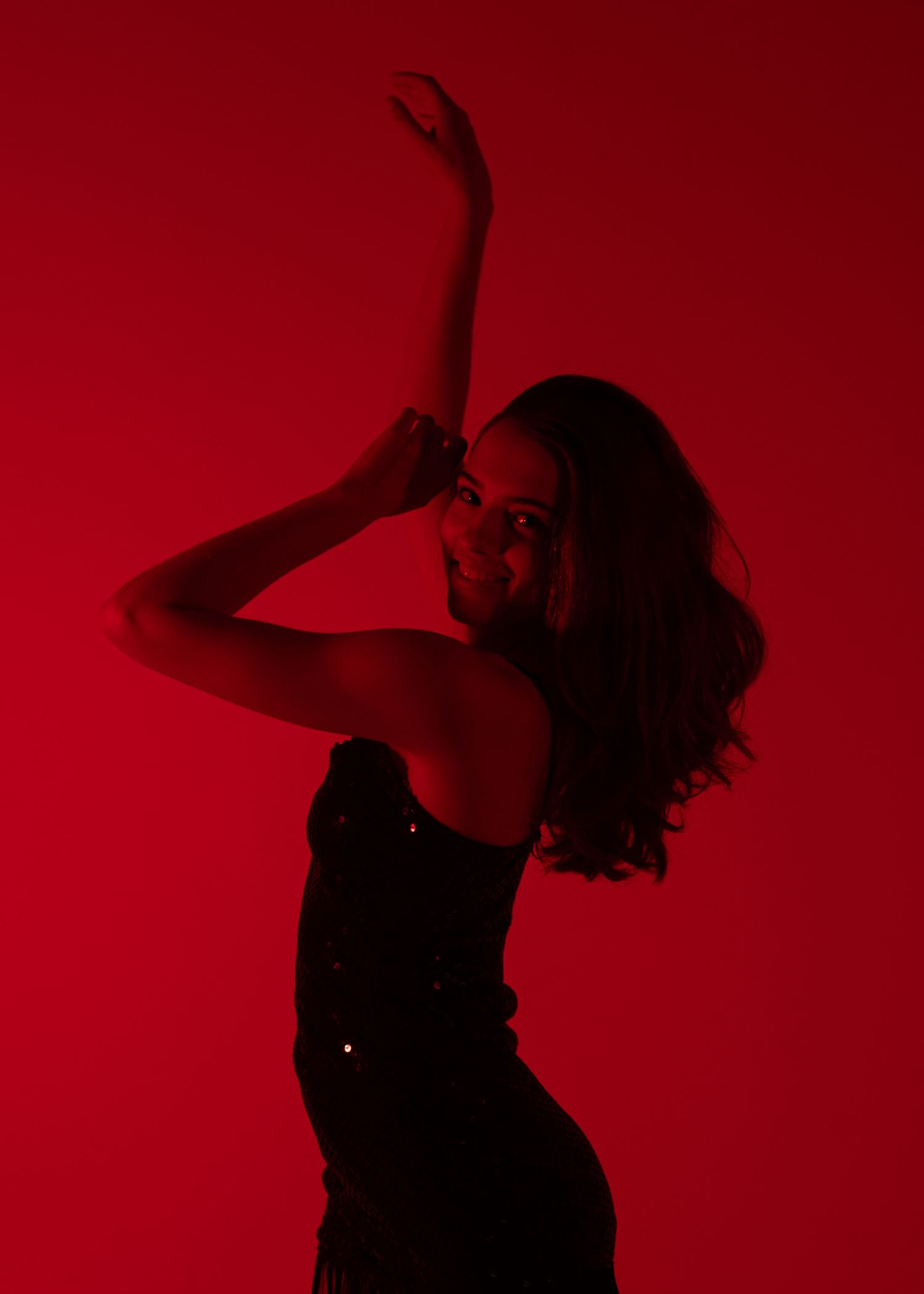 Dancer poses dramatically against a red background with one arm raised in artistic red-lit silhouette.