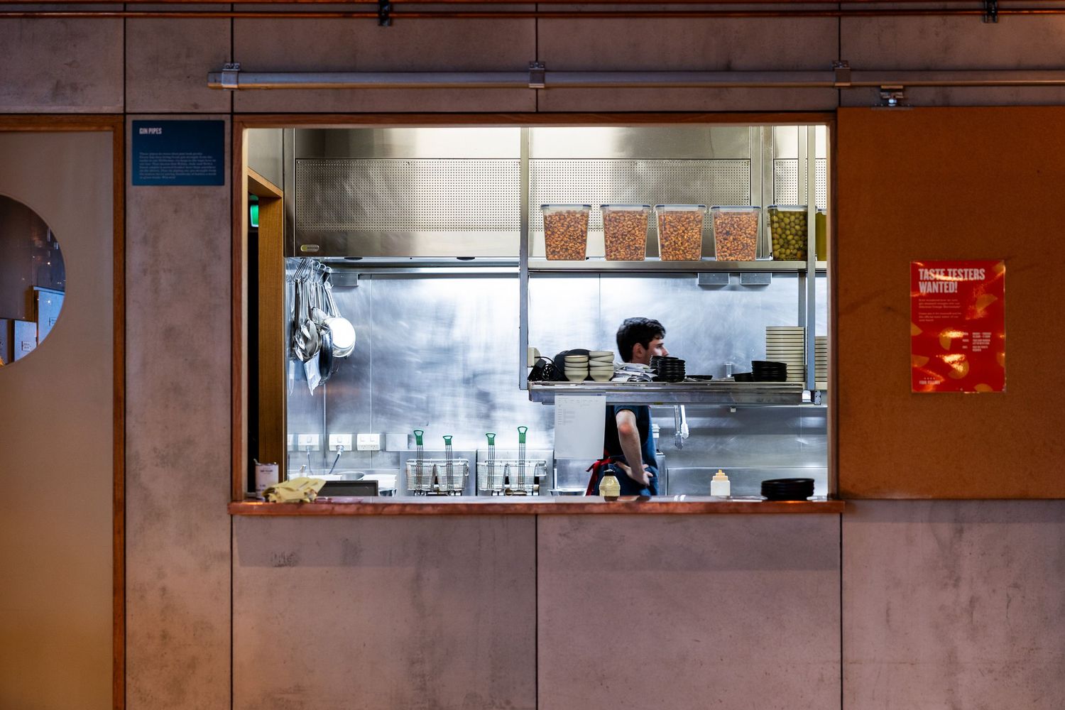 A chef working in an open kitchen viewed through a service window in a modern restaurant.