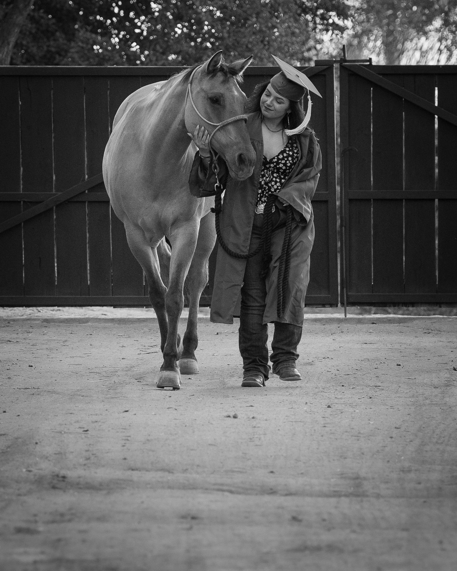 Black and white photo of woman in hat walking alongside a light-colored horse in arena.
